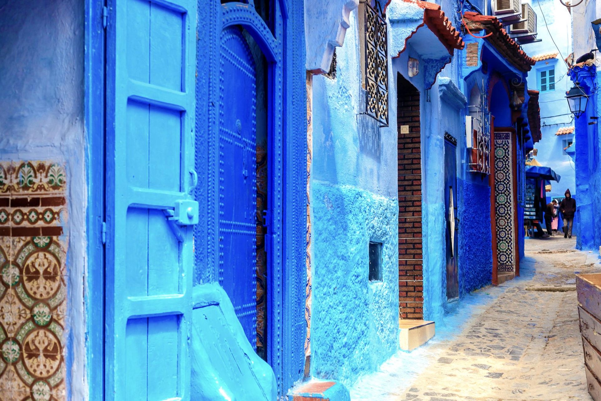A narrow cobblestone street in Chefchaouen, Morocco, featuring traditional blue painted walls and doors.