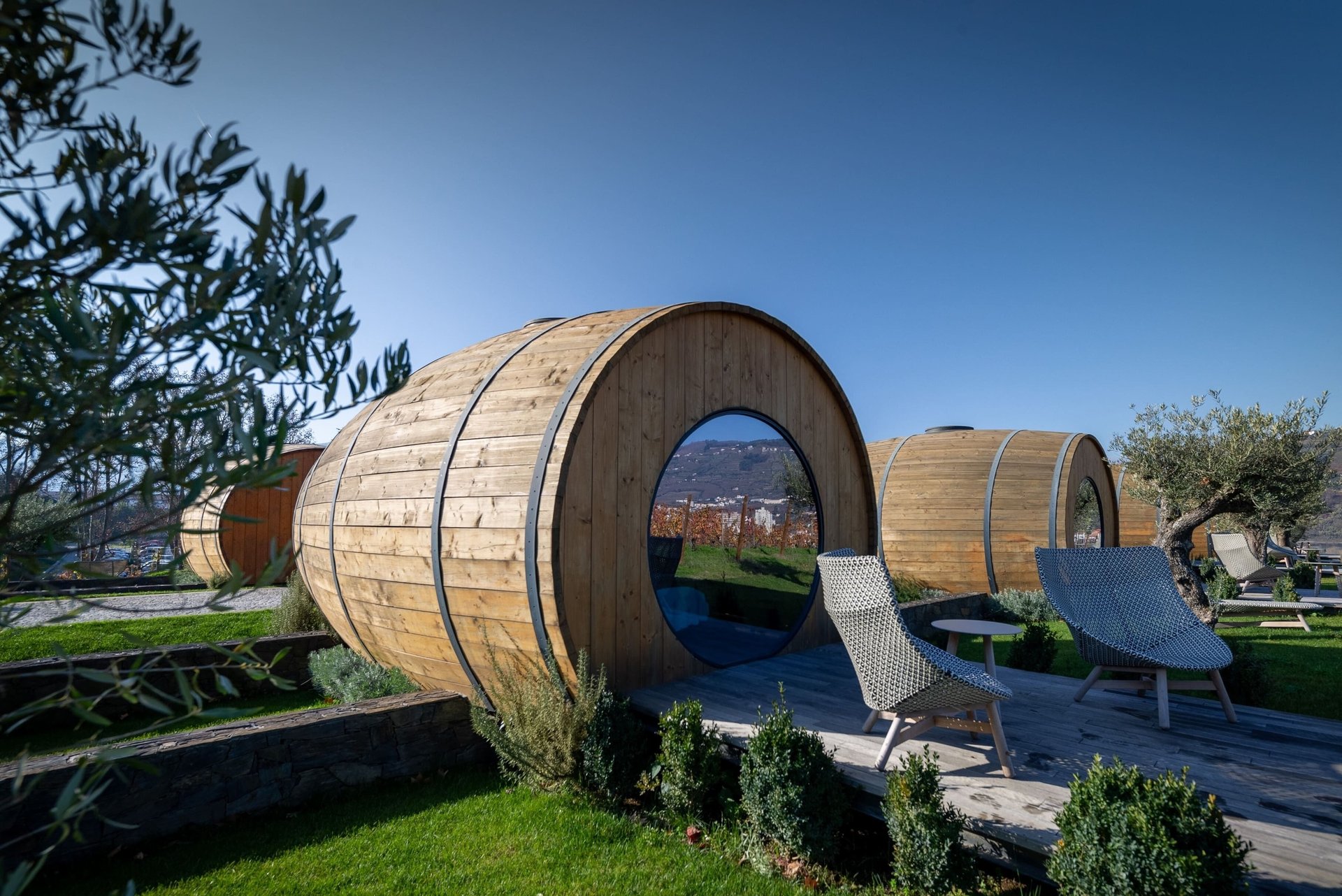 Luxury wine barrel hotel rooms with round windows and private decks overlooking a vineyard resort.