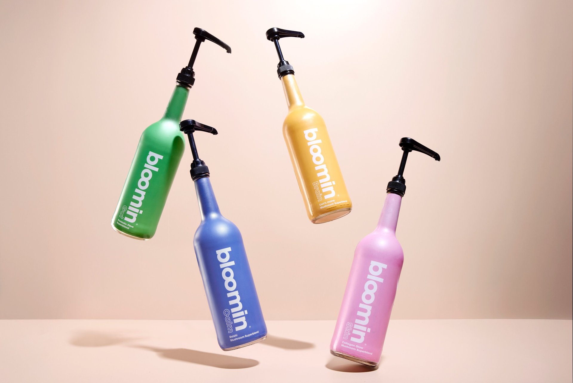 Vibrant product photography of colorful Bloomin pump bottles suspended mid-air against a warm beige