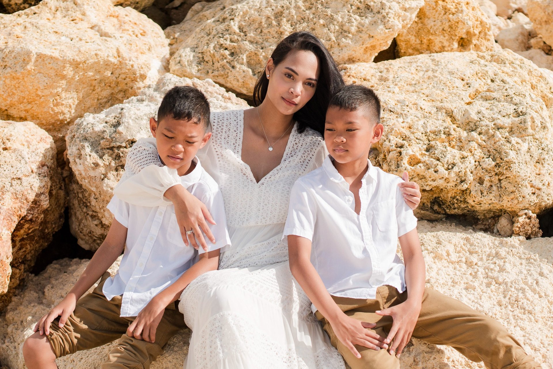 Ayunda mother with her two sons sitting by the rocks at Melasti Beach during a natural family photography session in Bali.