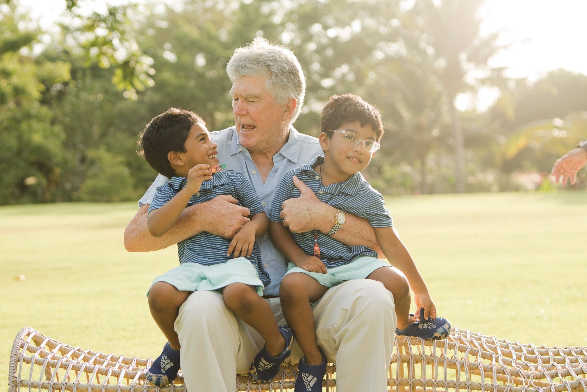 grandfather sitting and hugging his grandchildren on a woven chair at rimba by ayana bali during relaxed family photography