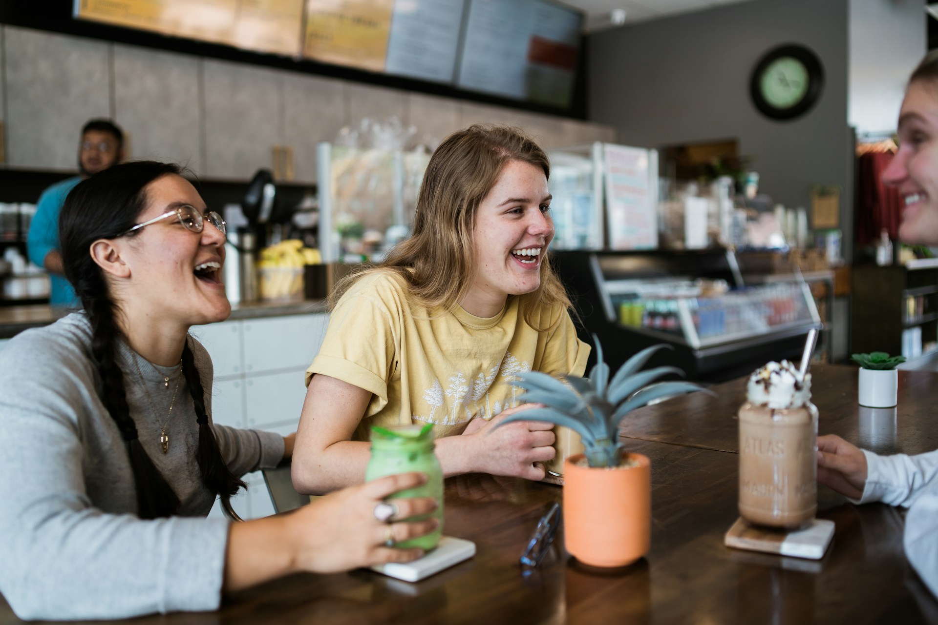 Dos jóvenes sonríen y conversan en una cafetería moderna, disfrutando bebidas y representando la cul