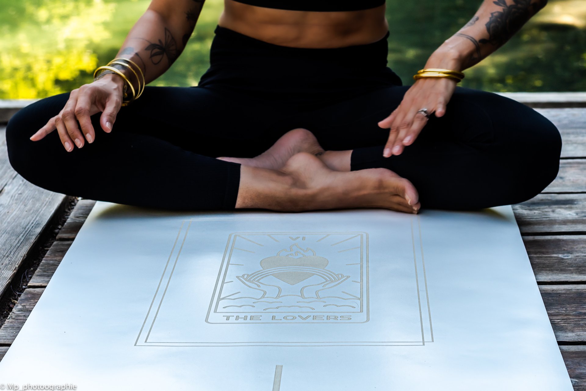 A woman sitting in a cross-legged yoga pose on a white yoga mat featuring The Lovers tarot card design.