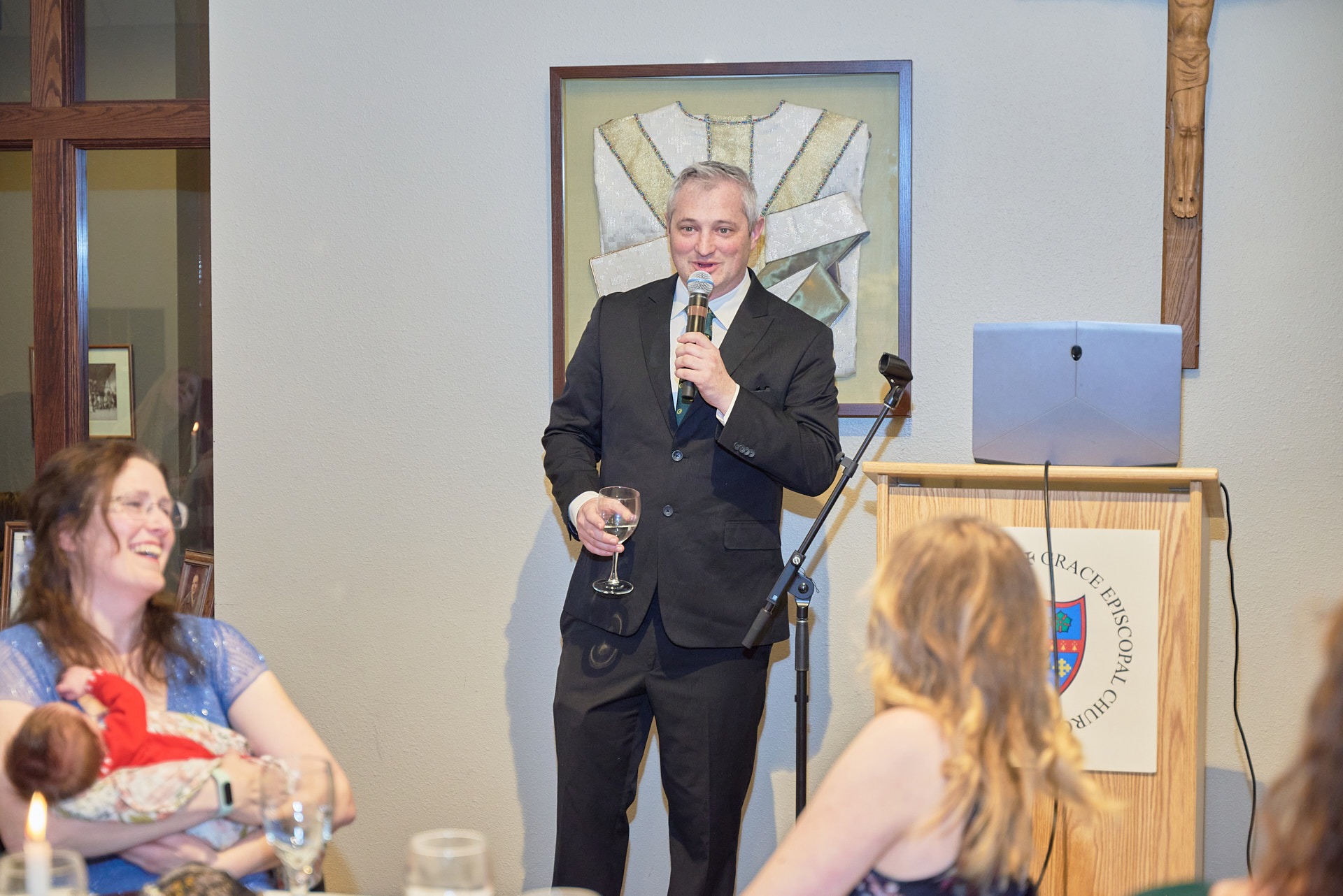 A man in a suit giving a speech toasting at a 50th anniversary party at Grace Episcopal Church.