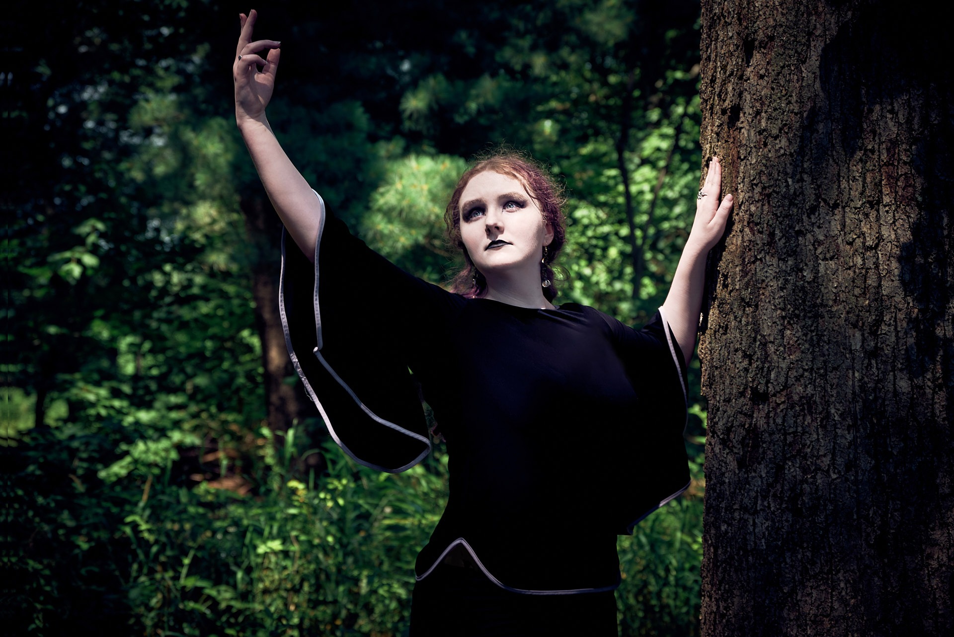 a woman in a black dress standing next to a tree dancing in the sunlight