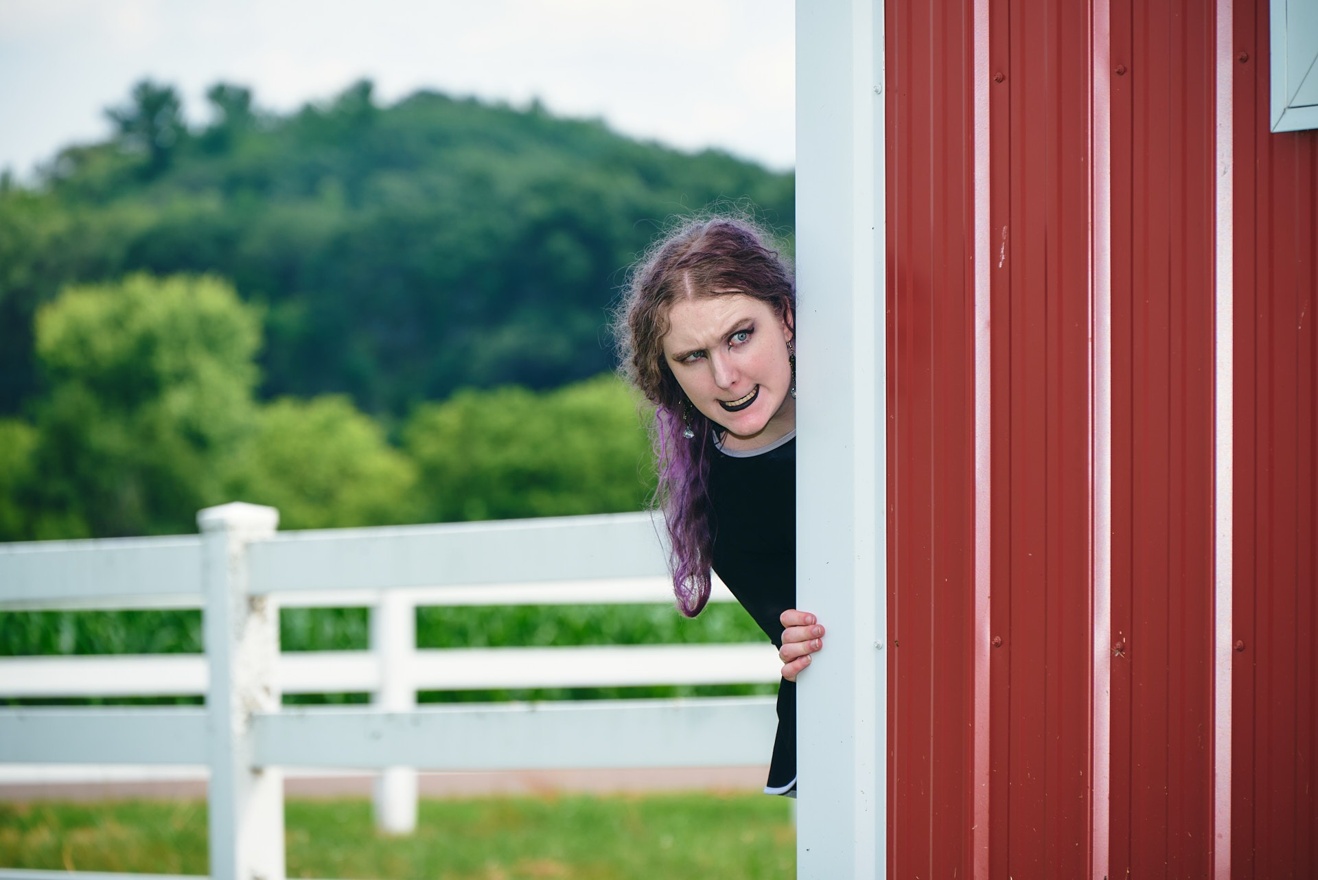 a girl with purple long hair looking out over a barn house with evil expression