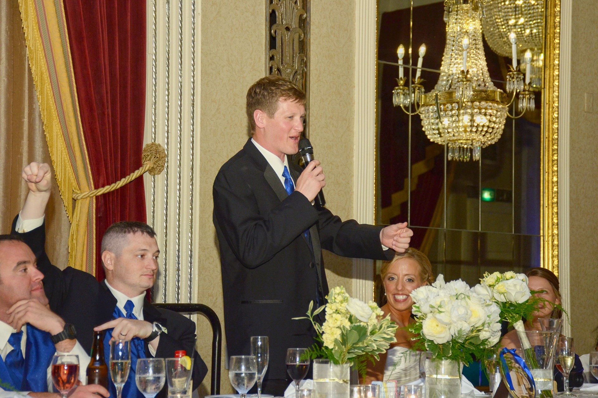 a groom giving a speech to the audience at the head table in a wedding