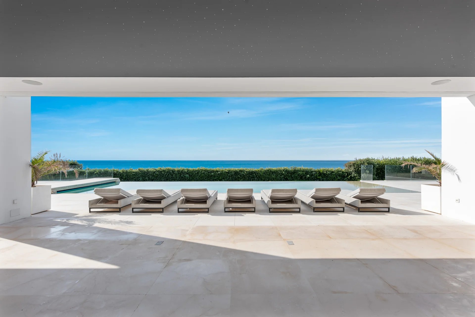 Luxury poolside patio with lounge chairs overlooking a modern infinity pool and the blue ocean.
