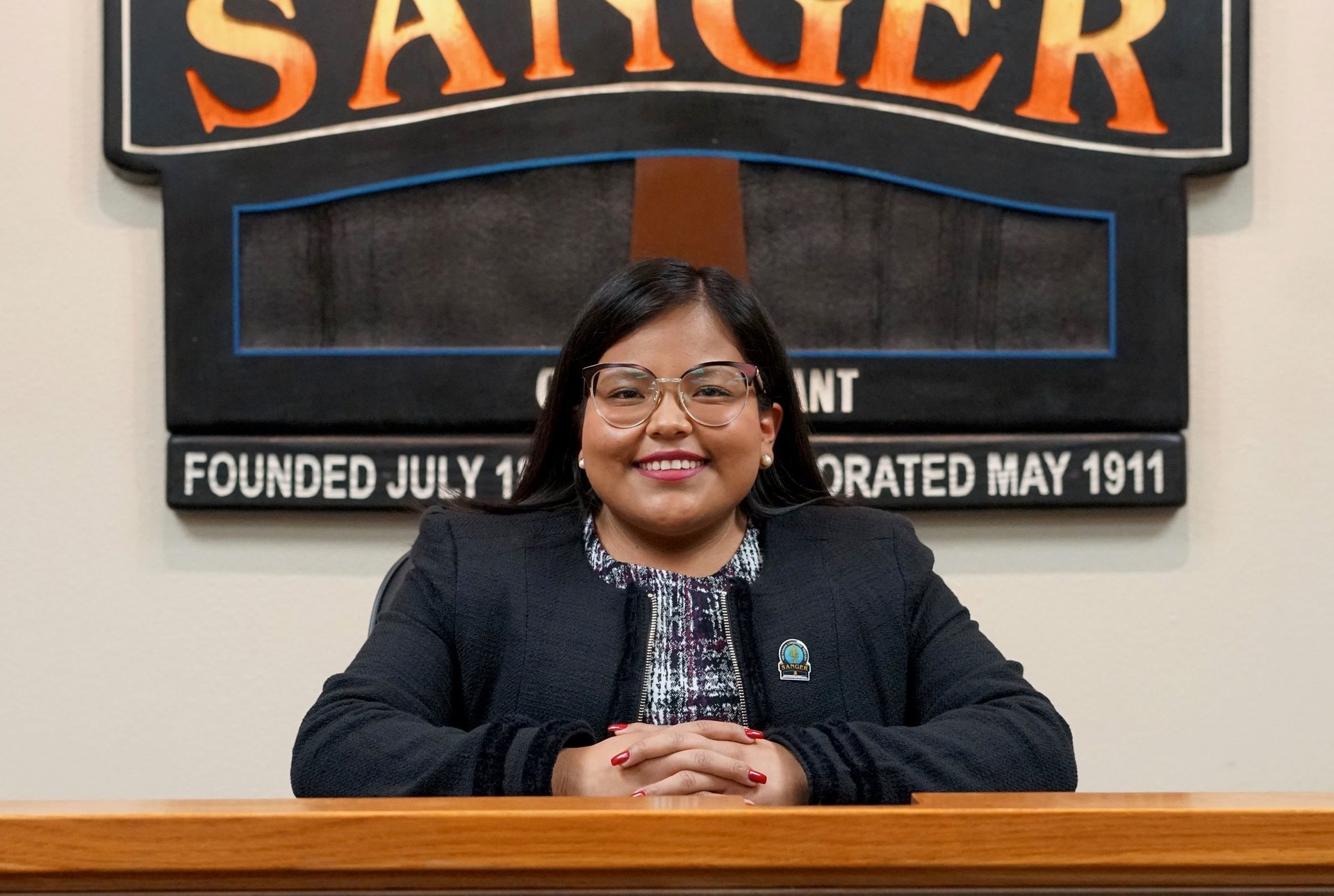a woman in a black jacket and glasses sitting at a podium
