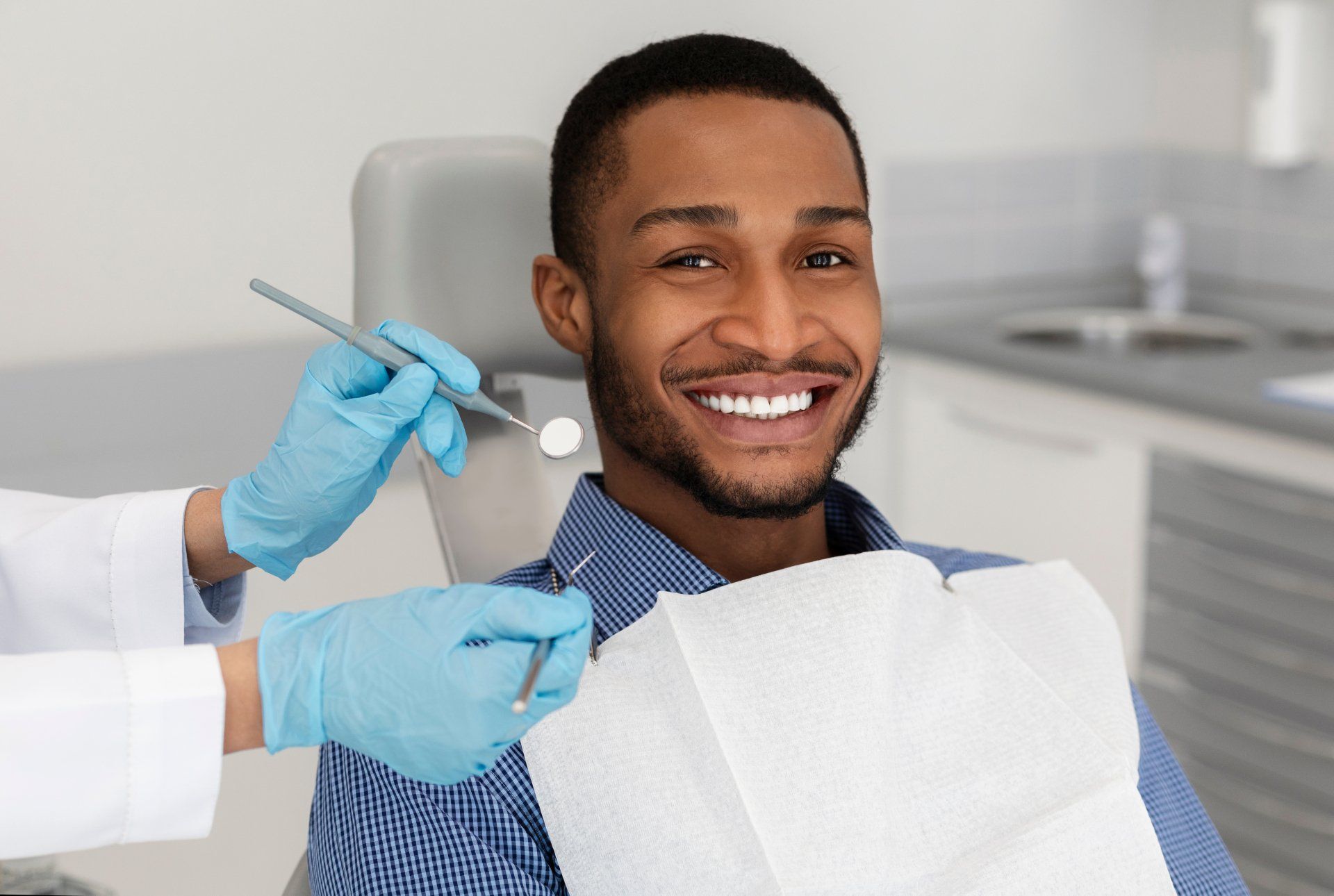 A smiling man as a dentist holds instruments nearby.