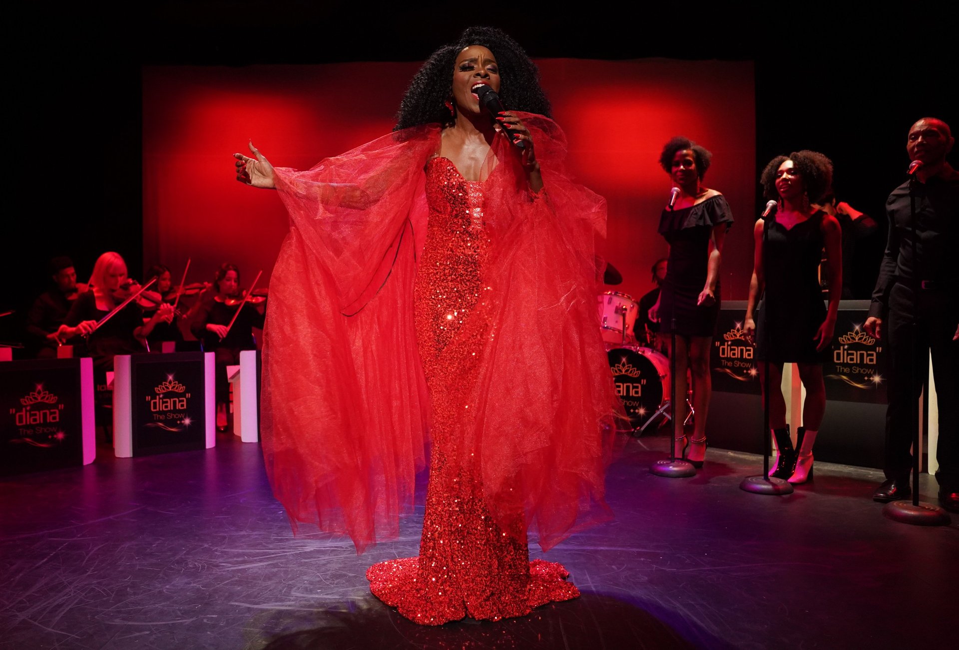 a woman in a red dress and an entire band with backup singers in the background