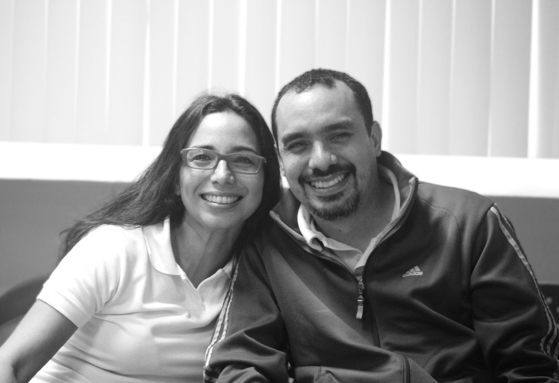 Un hombre y una mujer sentados uno junto al otro en un sofá, sonrientes miran la cámara