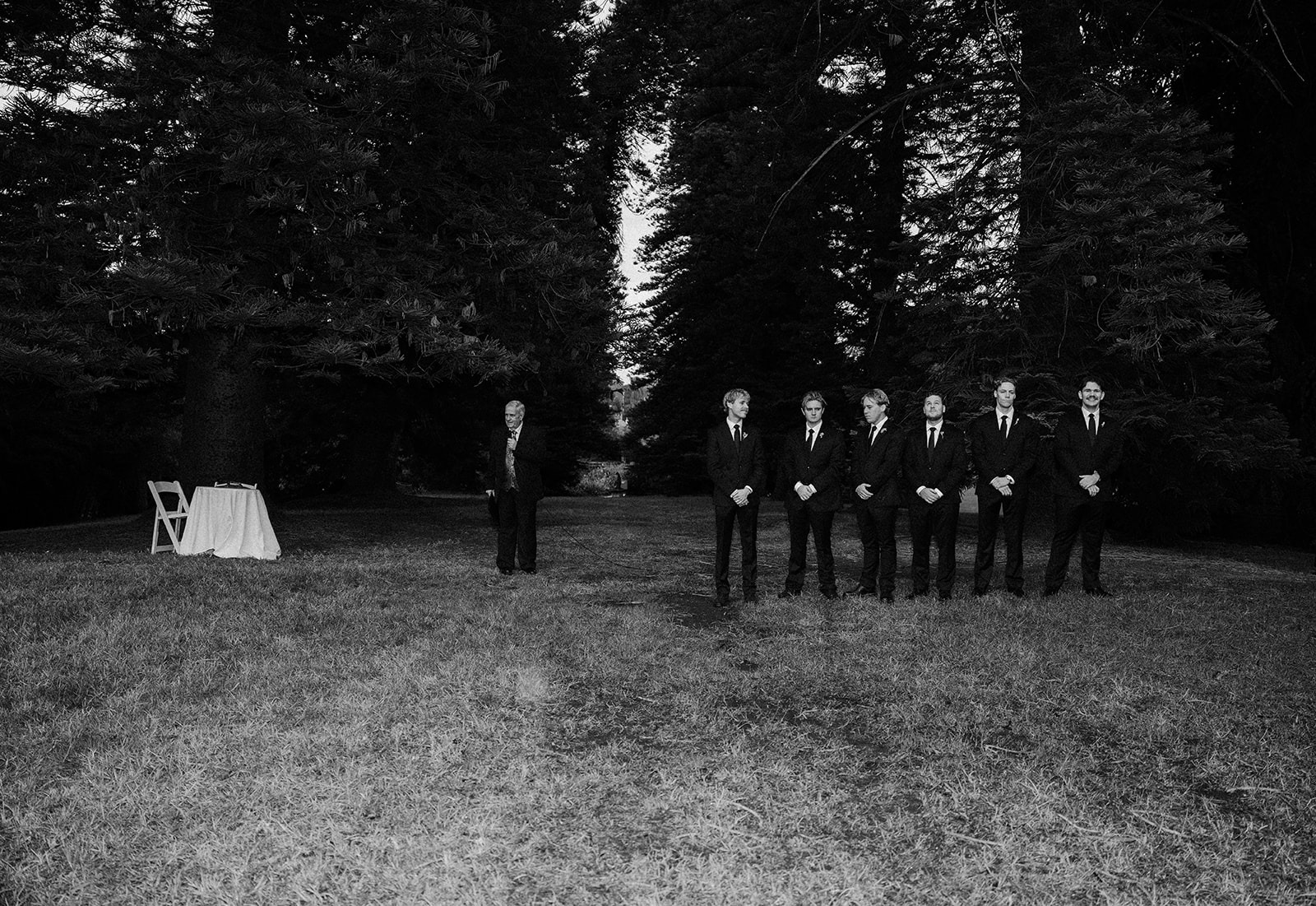 Groom and groomsmen in black suits standing in a forest for a woodland wedding ceremony.