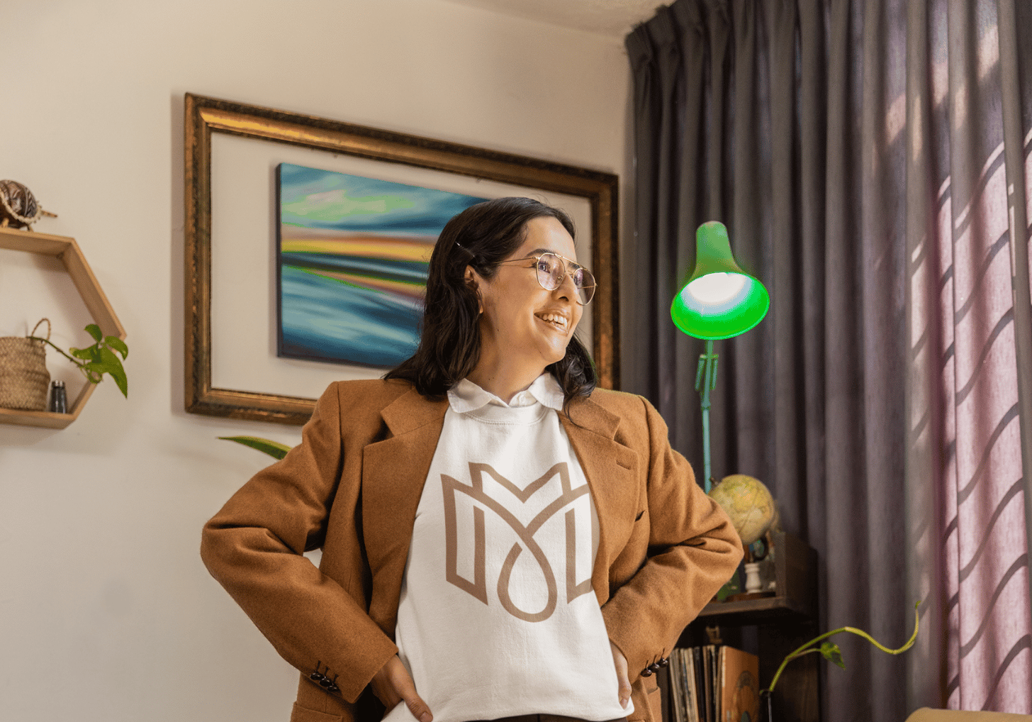 Femme souriante en veste marron et un sweat-shirt arborant un logo monogramme debout dans un bureau.