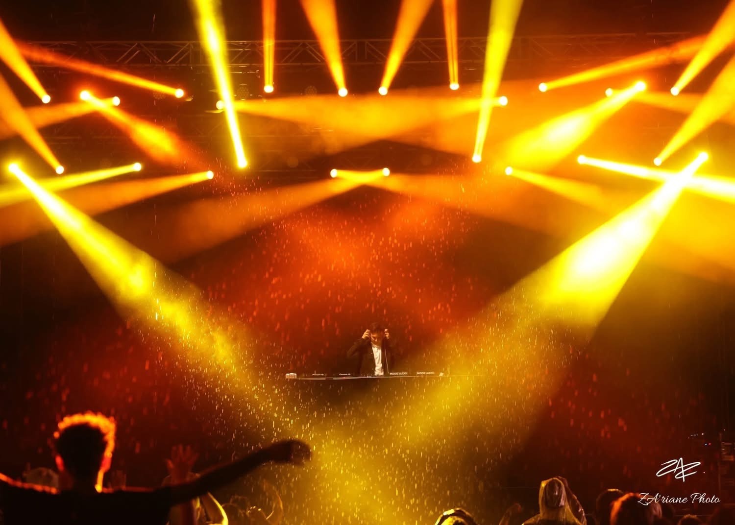 A DJ performs at a live music concert with dramatic golden stage lighting and special effects.