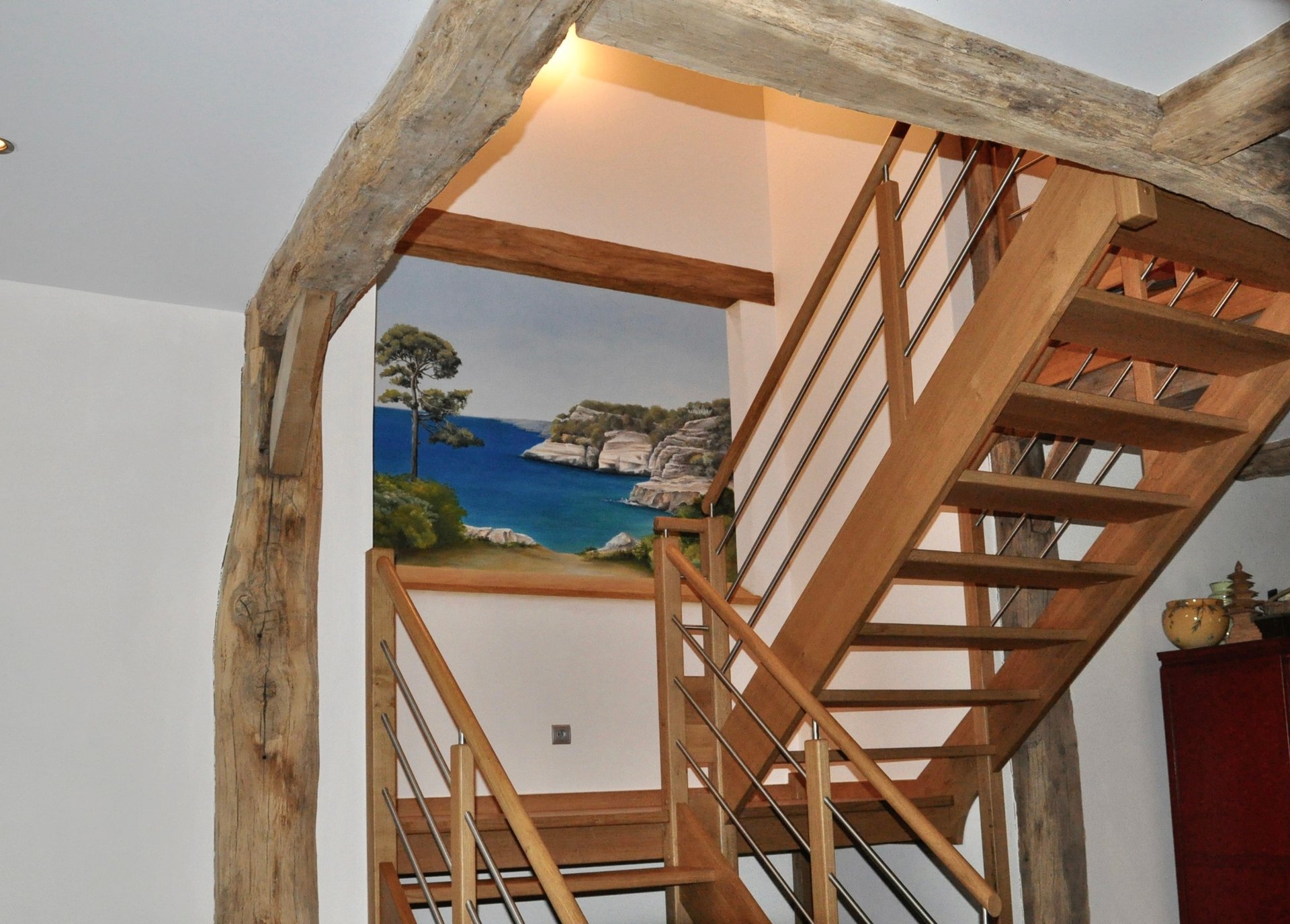 Une ouverture en trompe-l'oeil dans une cage d'escalier, invite au voyage en bord de mer. Le faux bois intègre l'ensemble.