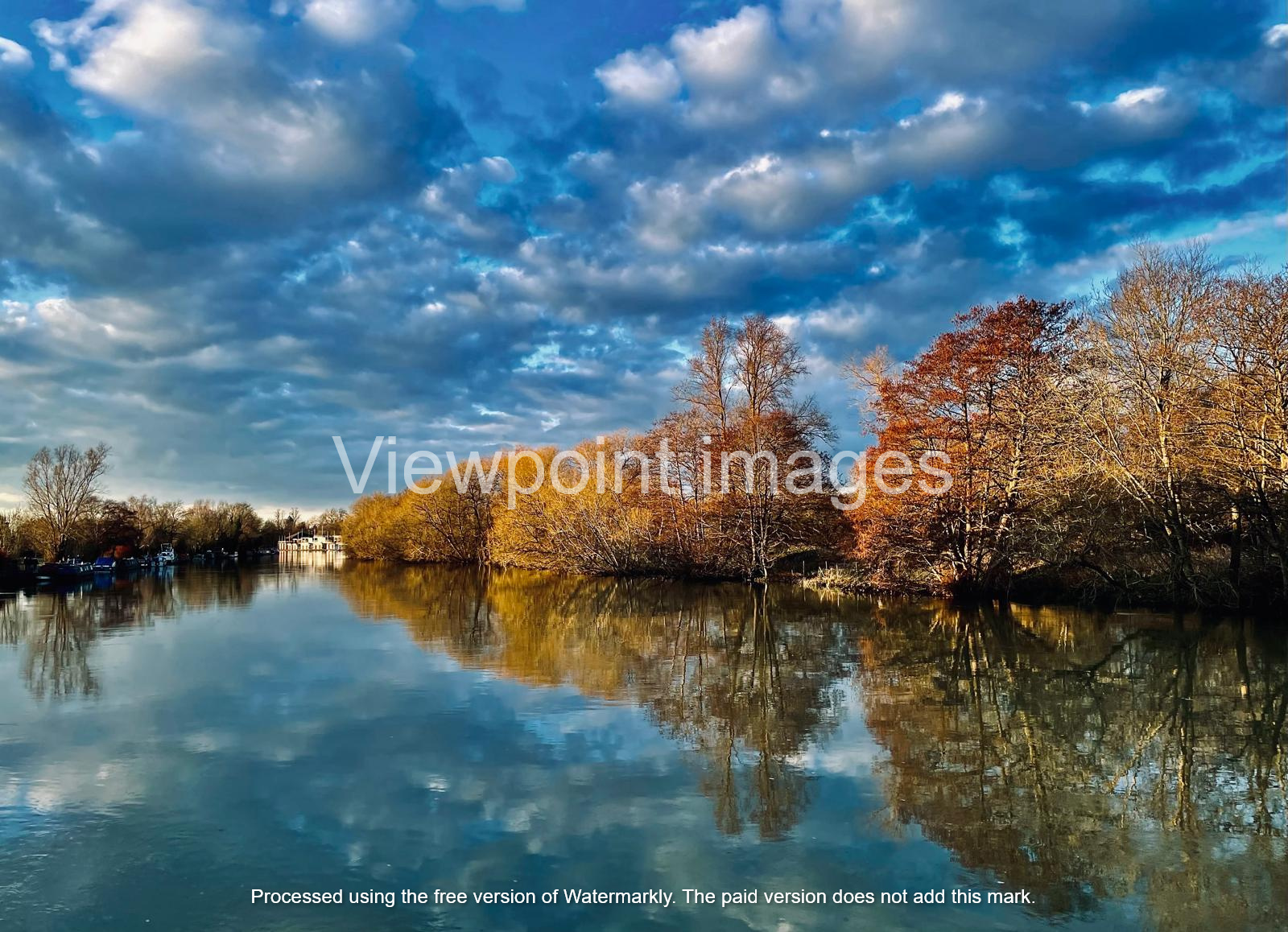 Tranquil river landscape with autumn trees reflecting in calm water under a dramatic blue sky.