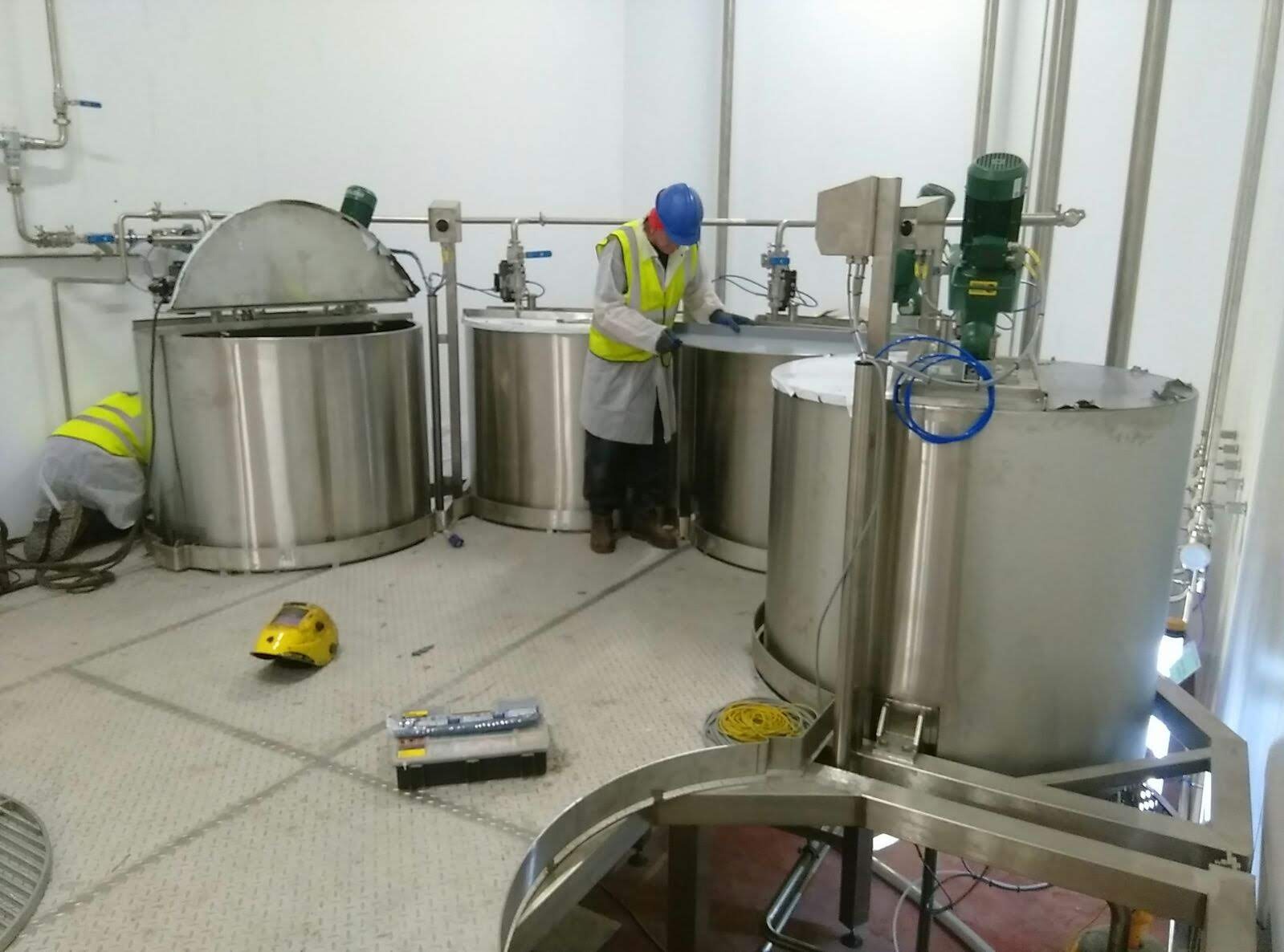 Industrial workers installing and maintaining stainless steel chemical mixing tanks in a factory.