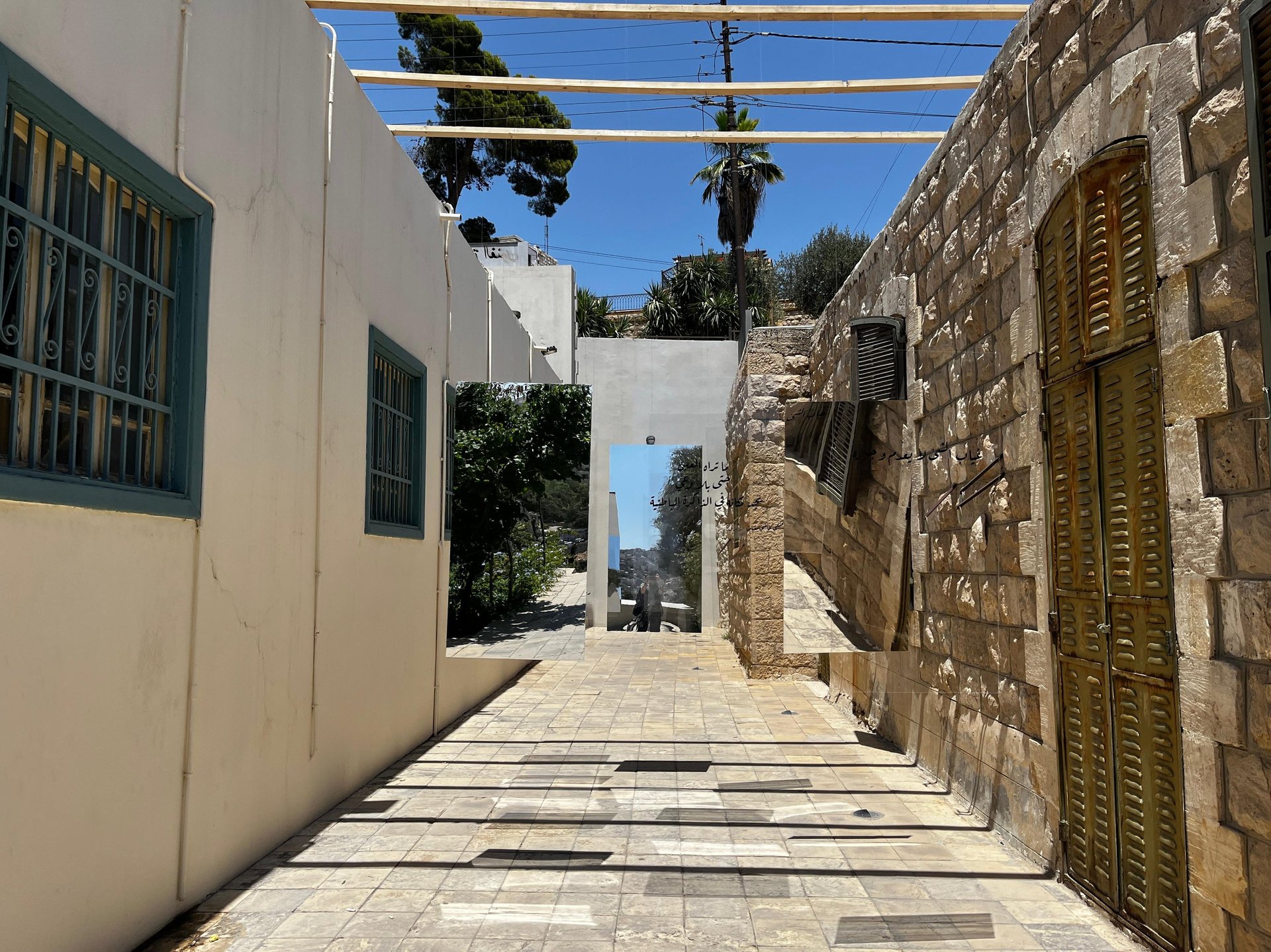 Mirrored art installation in a stone alleyway reflecting an outdoor scenery luminous space