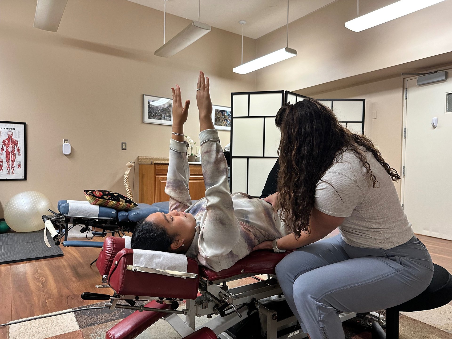 Chiropractor with hands on patients stomach and lower back, coaching form for rehab exercise.