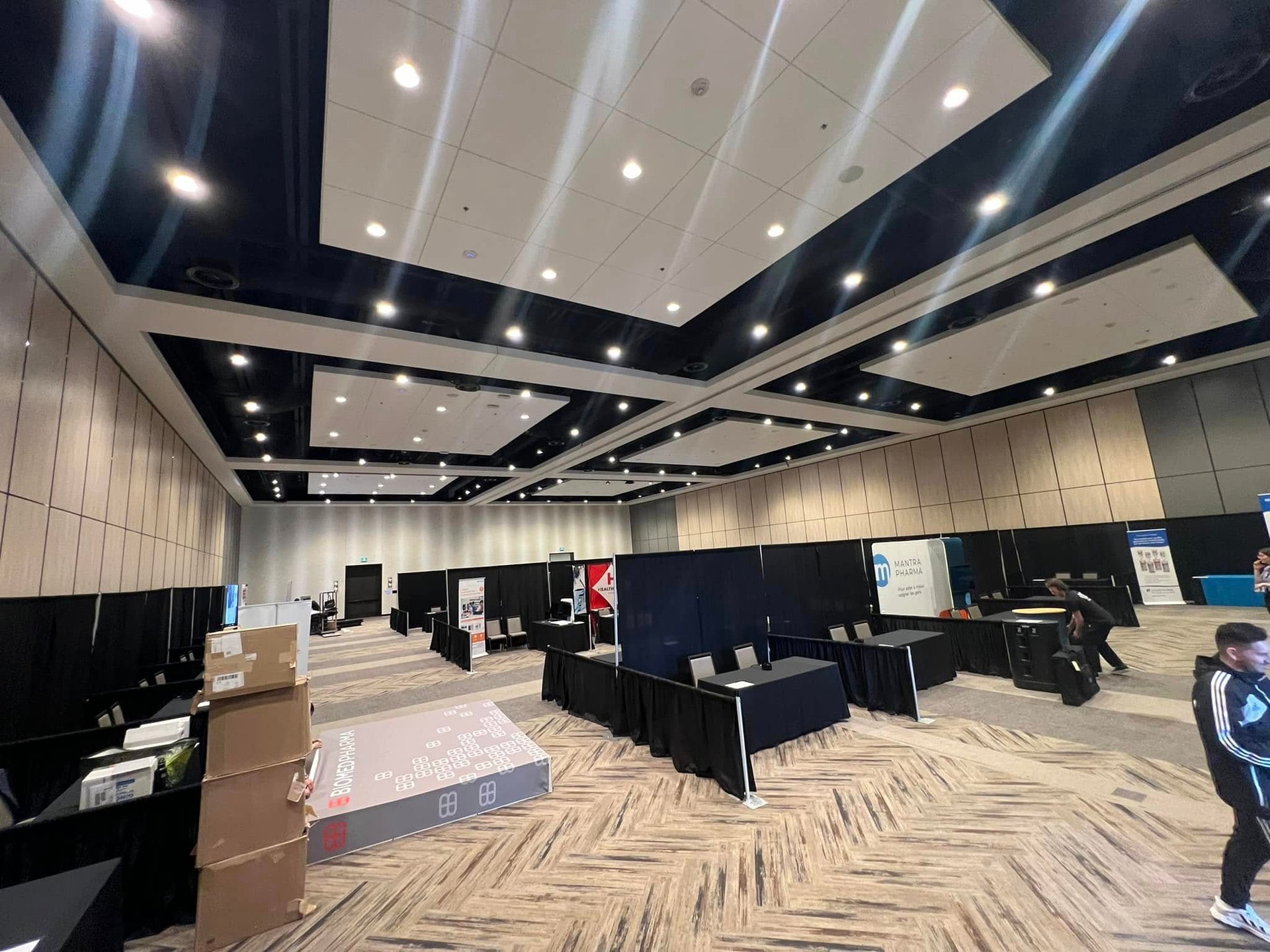 Professional trade show floor setup in a modern conference hall with black draped booths and event signage.