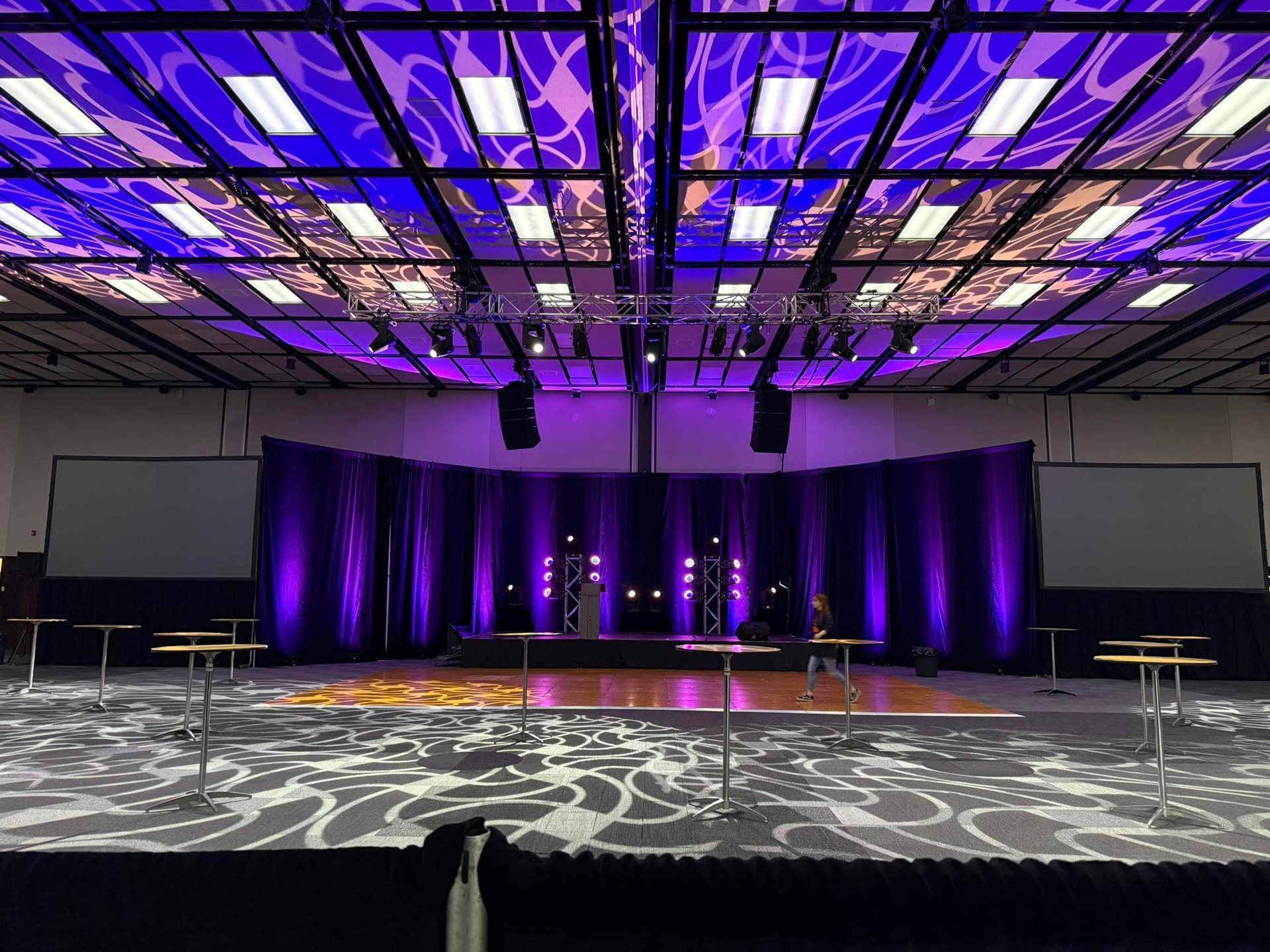 Grand ballroom event space with purple stage lighting, professional audio equipment, and high-top tables.
