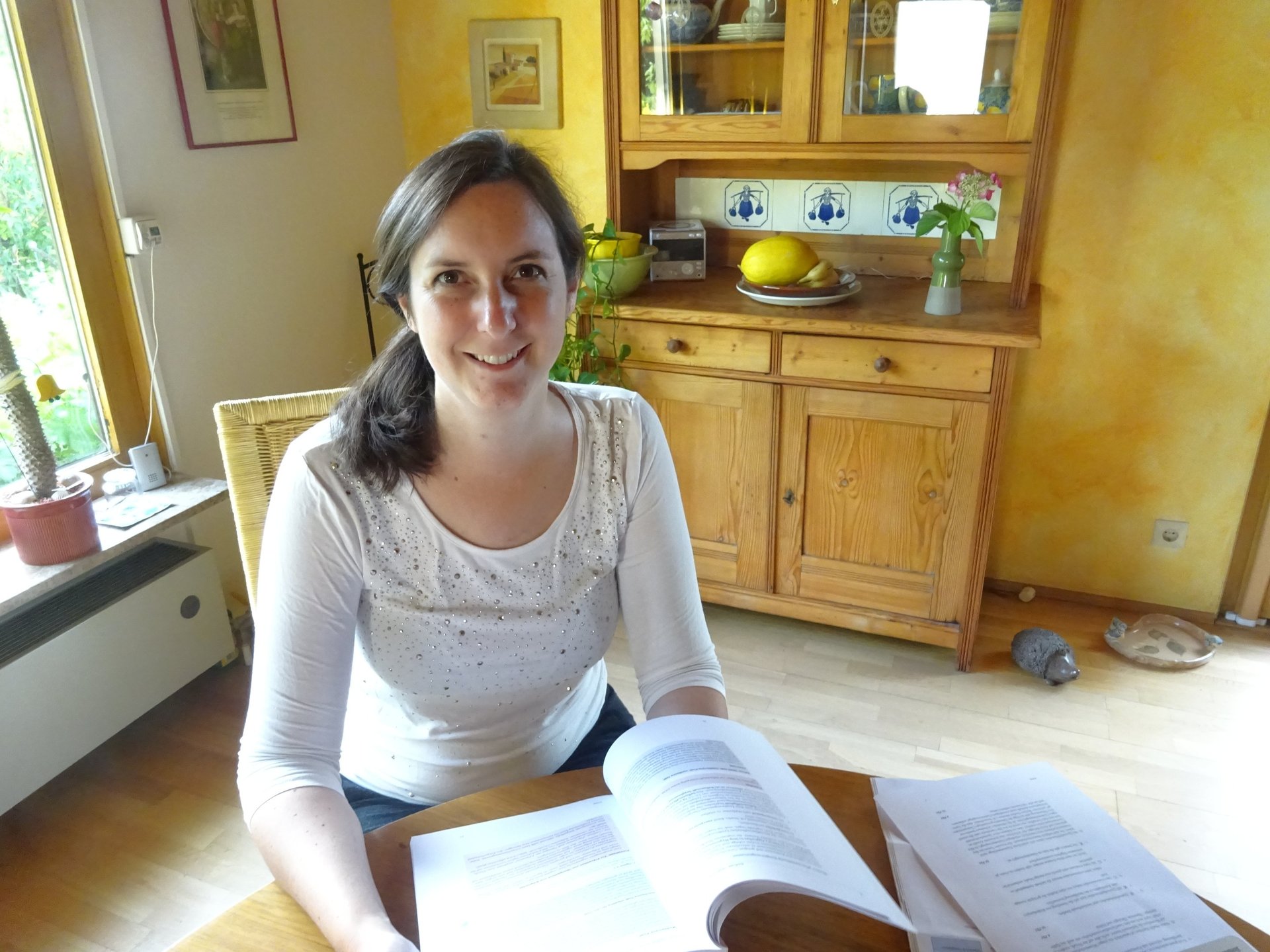a friendly smiling woman sitting at a table with a book