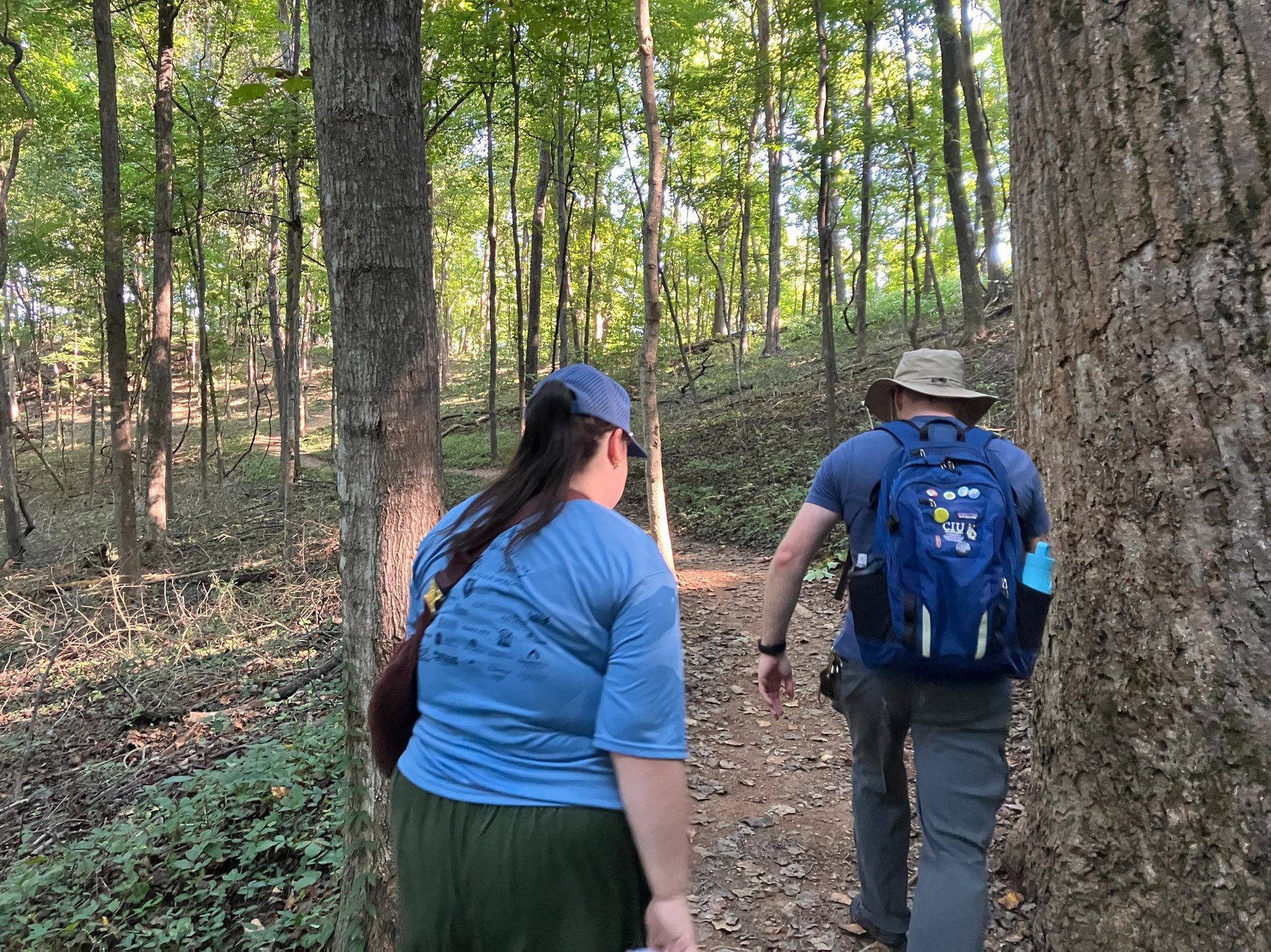 A man and a woman hike up the dirt path in the woods