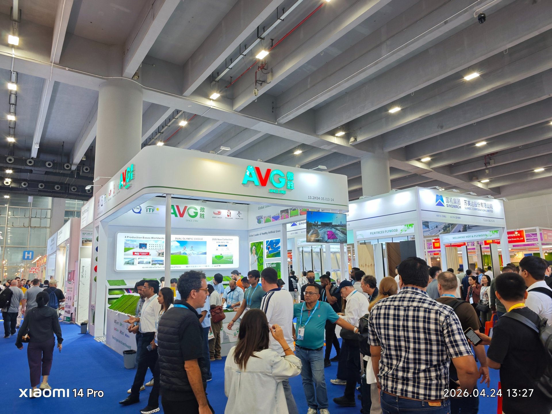 Crowded AVG artificial grass booth at a busy international trade show exhibition hall.