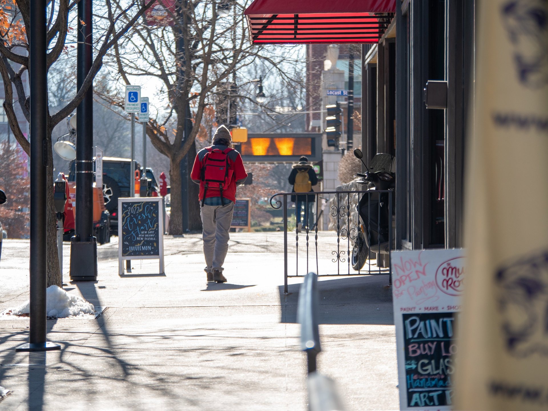 Man walking on a sidewalk downtown past business and sandwich signs