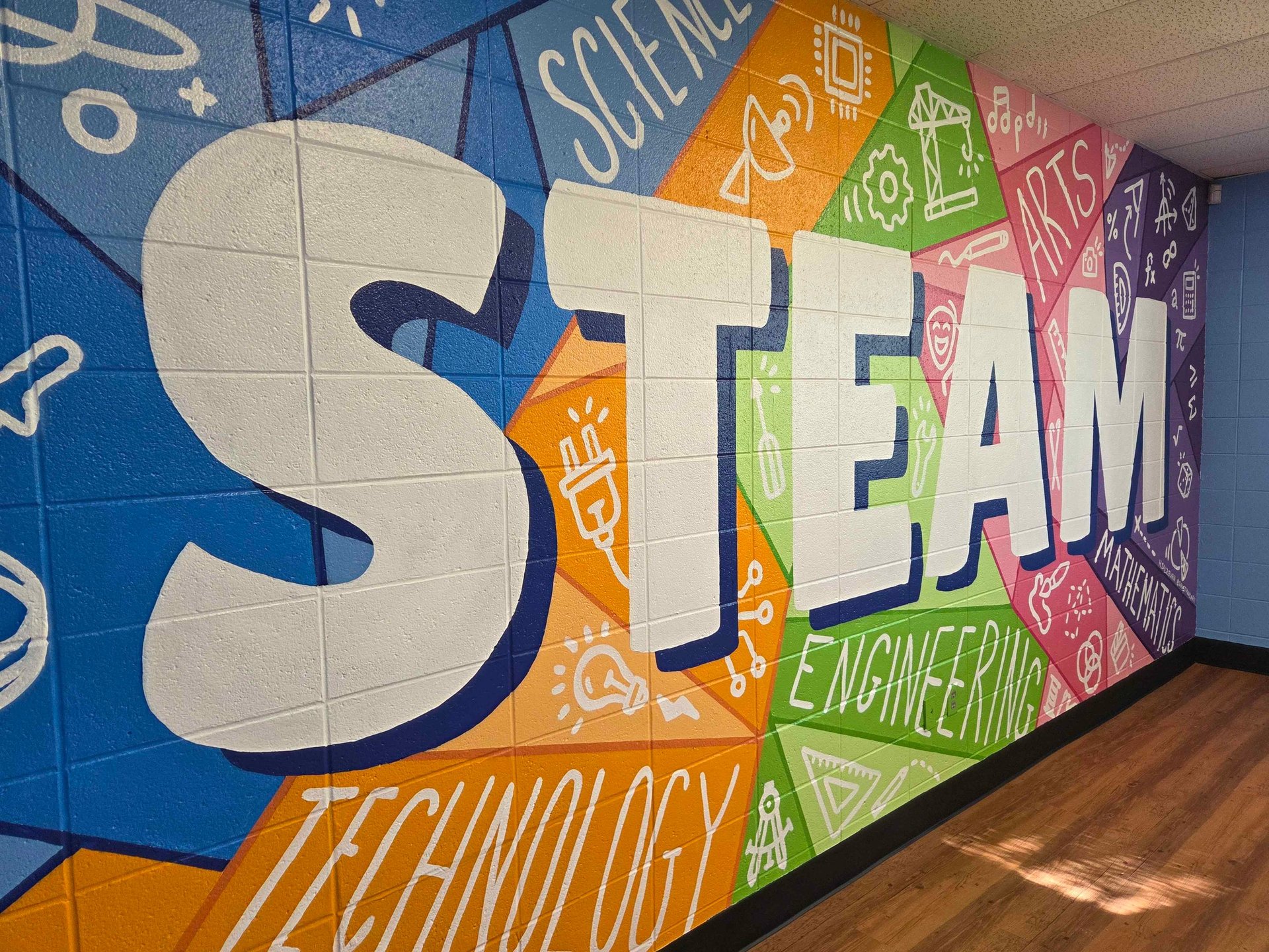 A colorful STEAM education mural on a brick wall featuring science, technology, engineering, arts, and math icons.