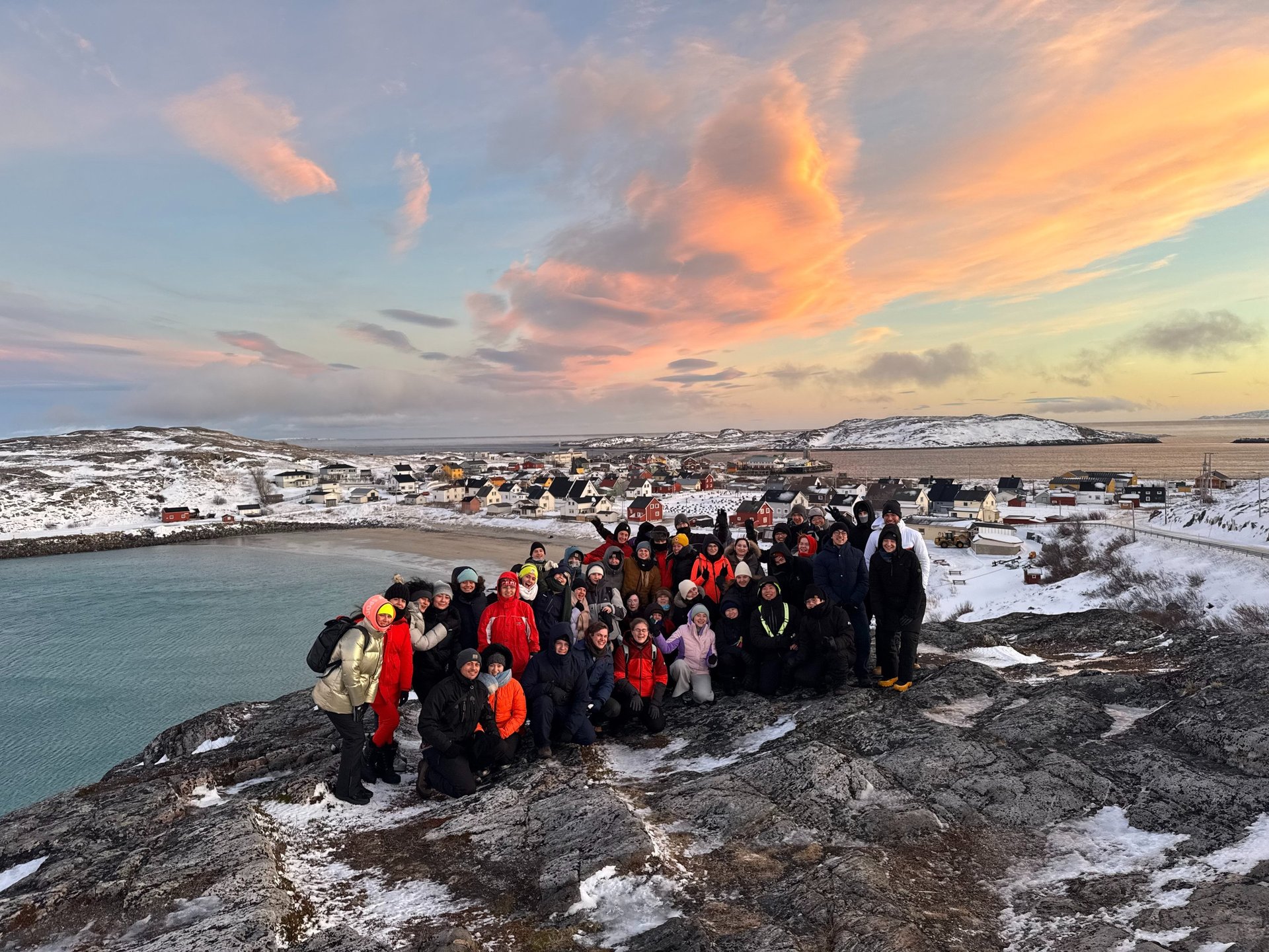a group of people standing on a rocky cliff with a beautiful pink sky in the nordics