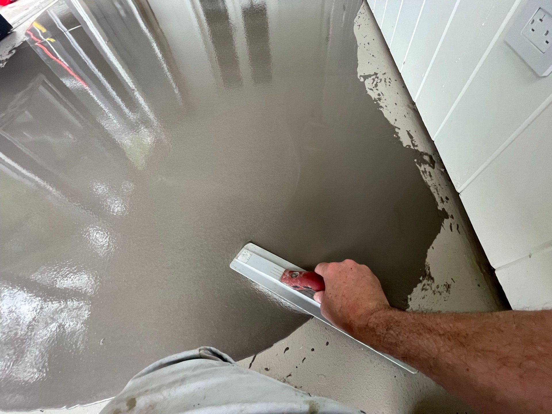 Pracownik rozprowadza masę samopoziomującą za pomocą pacy