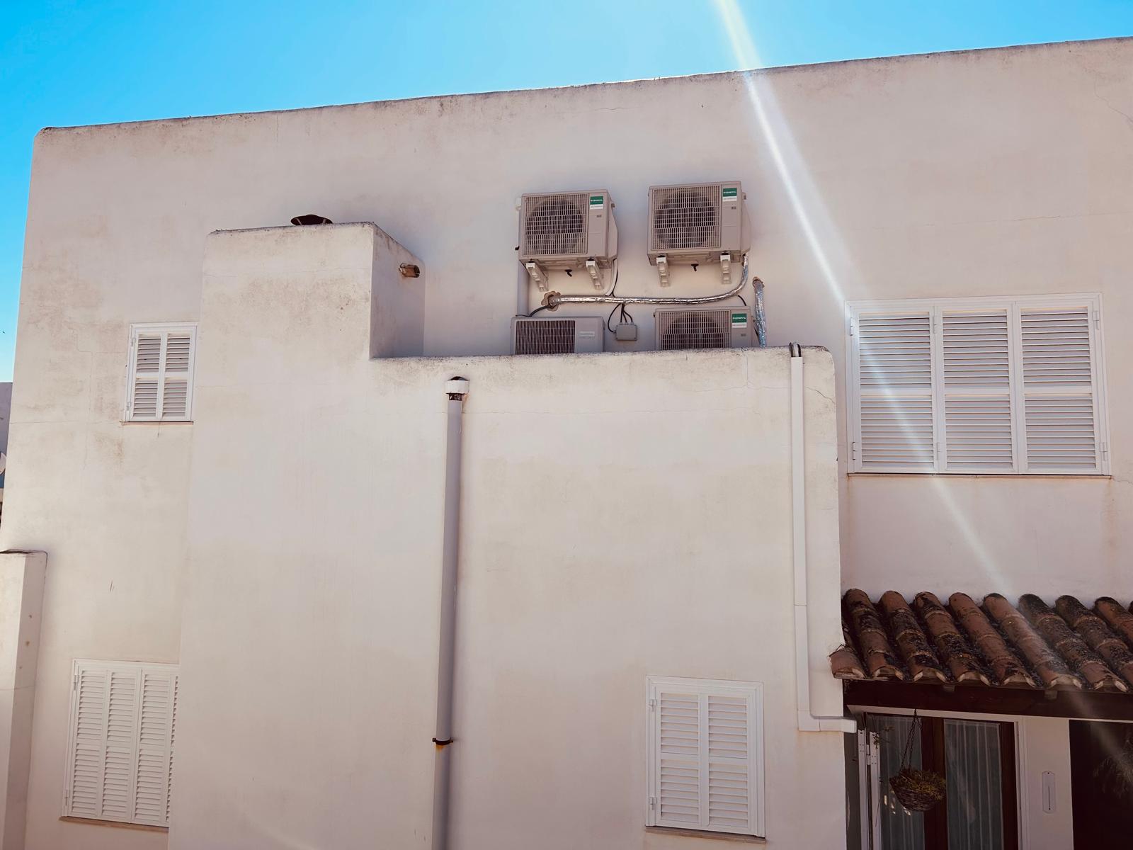 Outdoor HVAC air conditioning units mounted on a white Mediterranean building wall under a clear blue sky.
