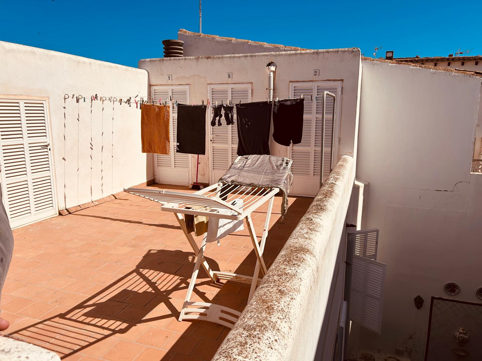 Laundry drying on a sunny Mediterranean rooftop terrace with a clothesline and folding rack.