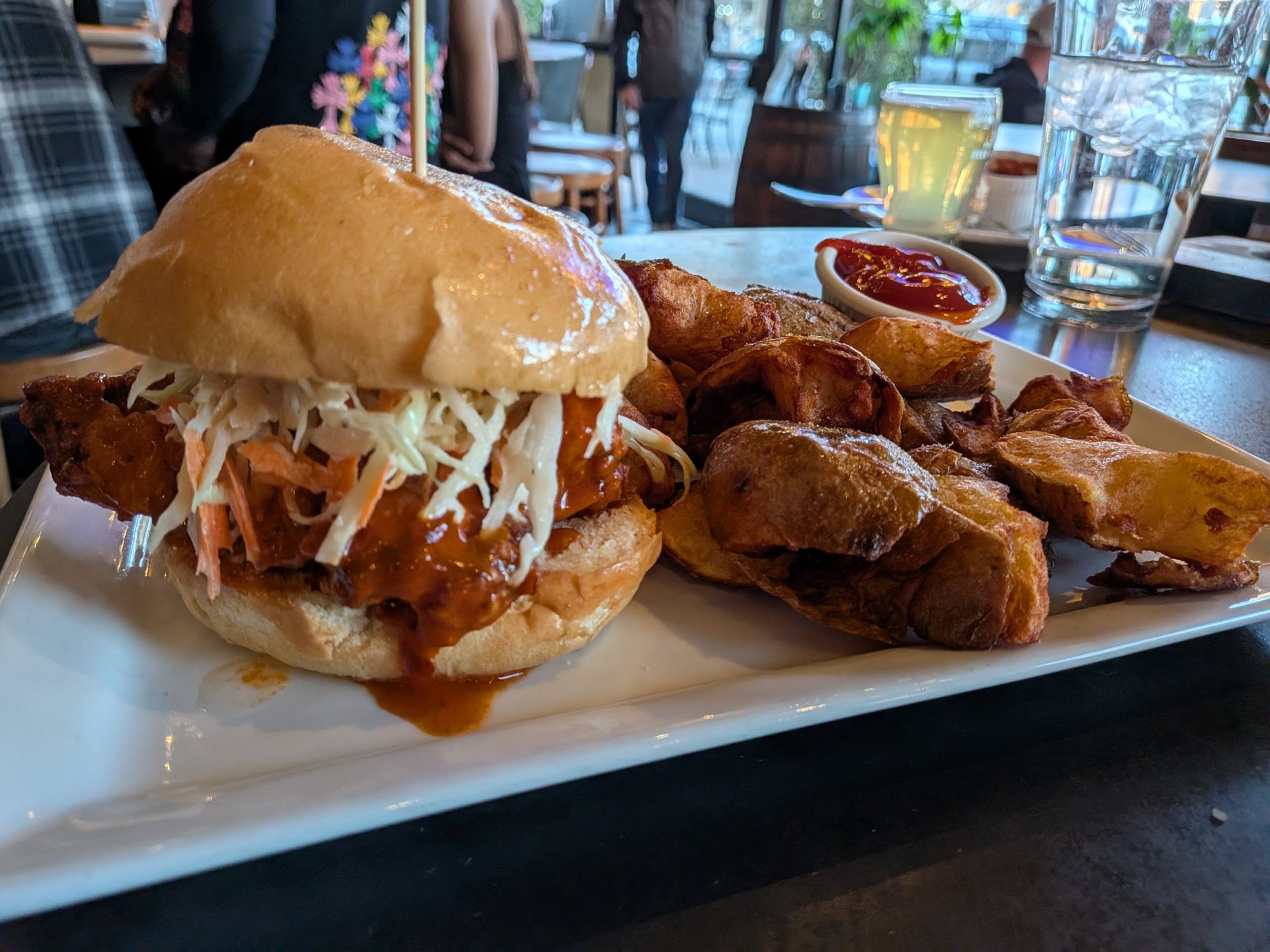 Crispy fried chicken sandwich with coleslaw served with potato wedges and ketchup on a white plate.