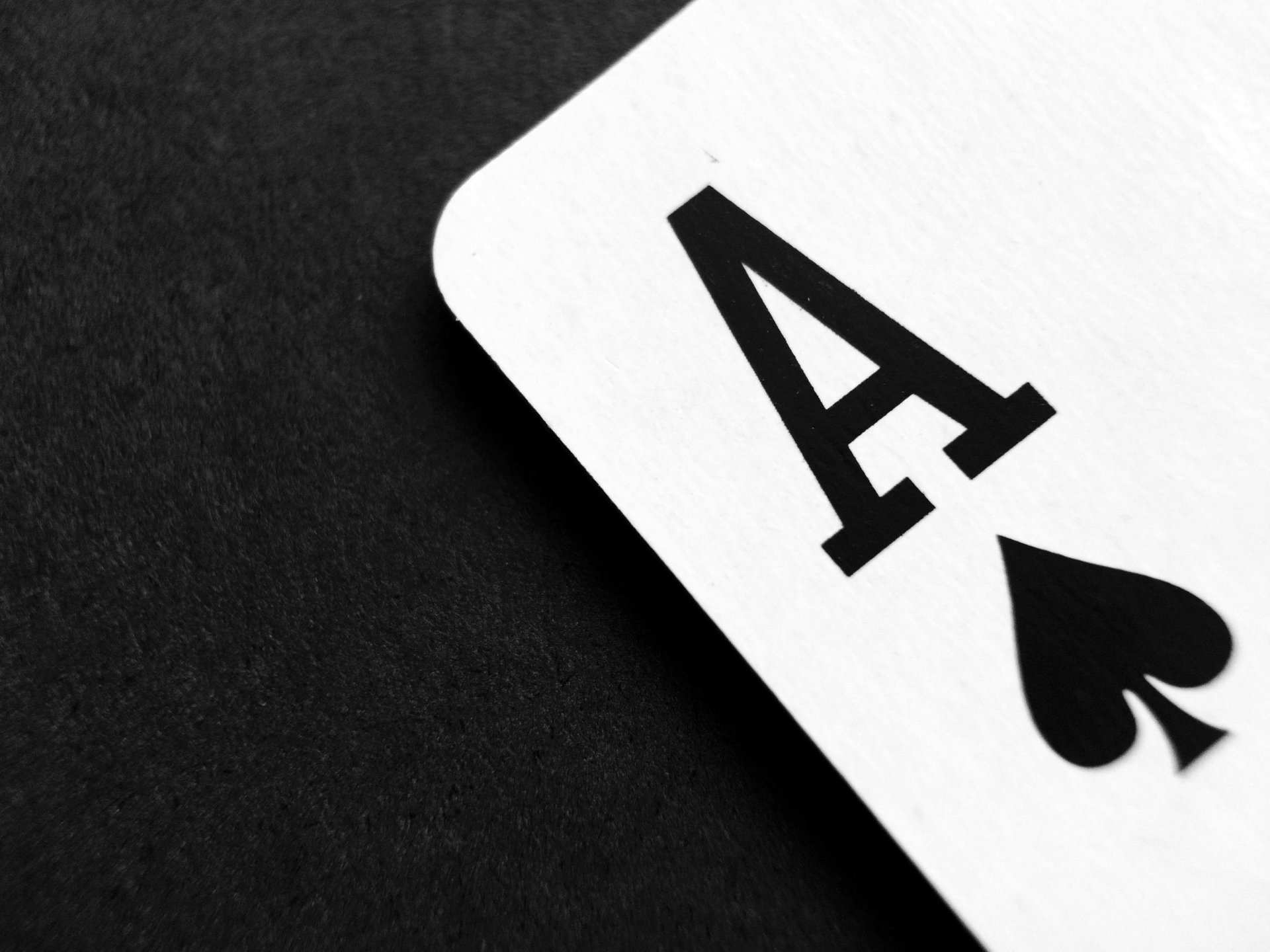 The corner of a playing card, the ace of spades, against a black fabric background.