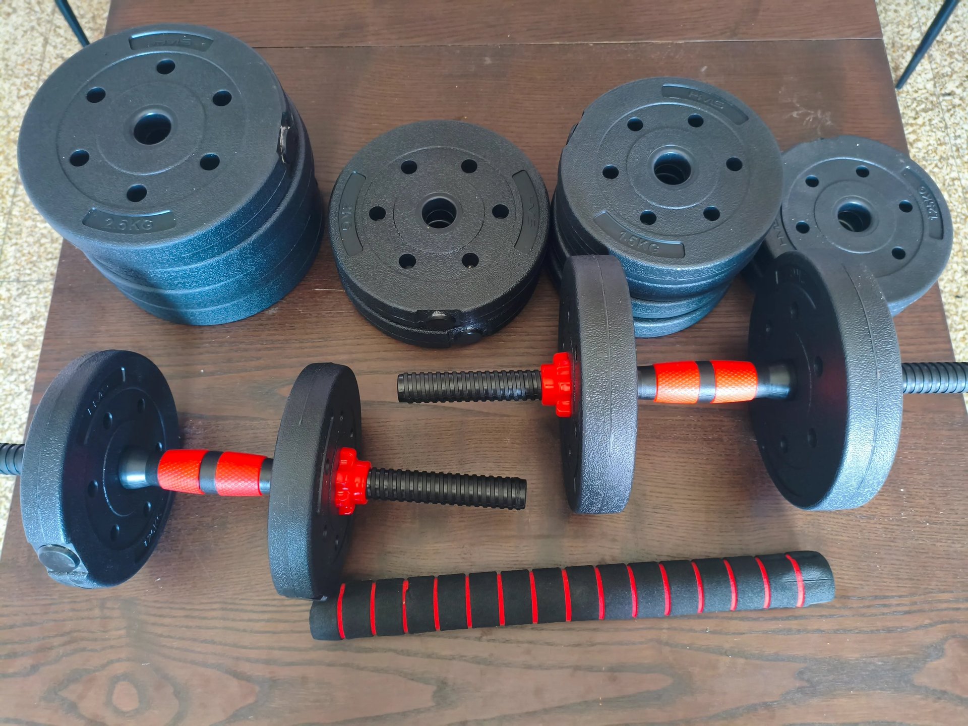 Kit de halteres ajustáveis JUPPLIES com discos pretos e punhos com detalhes vermelhos numa bancada d