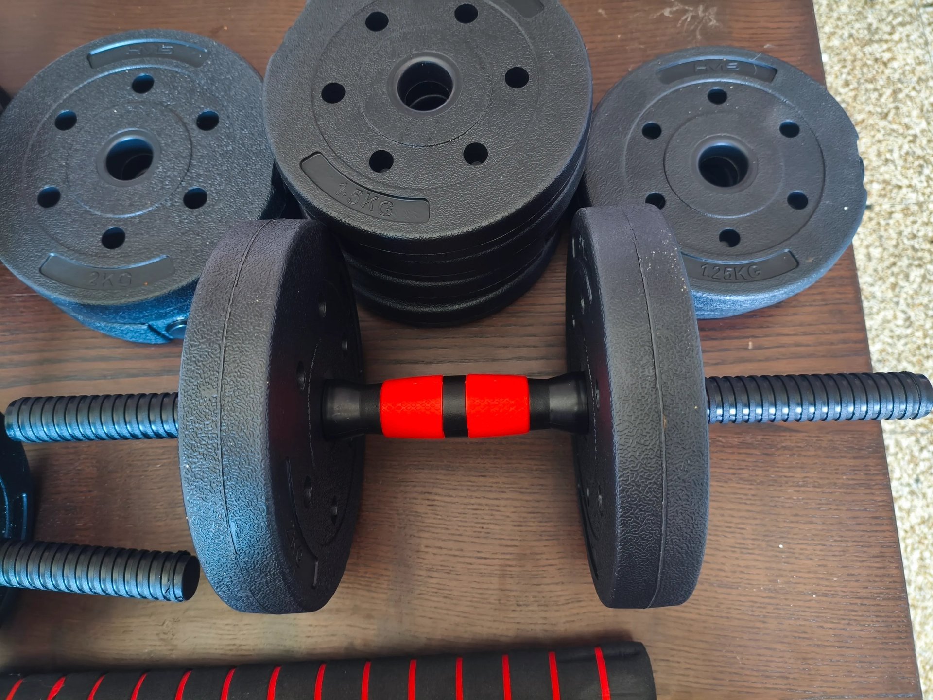 Detalhe do punho vermelho e preto dos halteres ajustáveis JUPPLIES com discos de peso empilhados