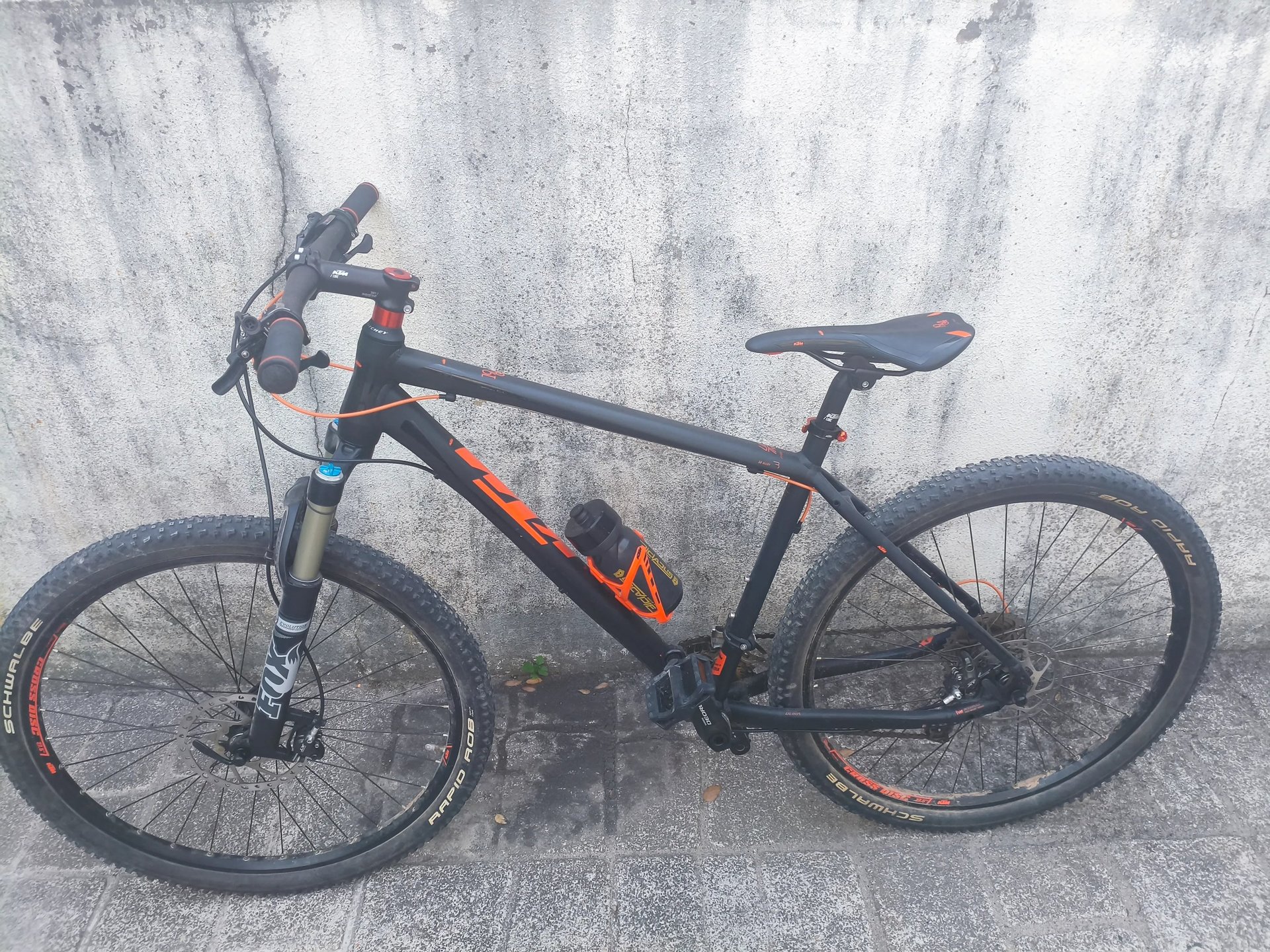 Bicicleta de montanha KTM preta com detalhes a laranja, quadro hardtail e pneus largos, vista latera