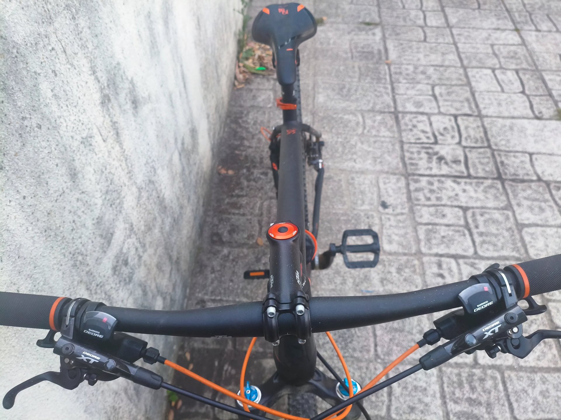 Bicicleta com detalhes a laranja fotografada de cima, junto a parede de pedra