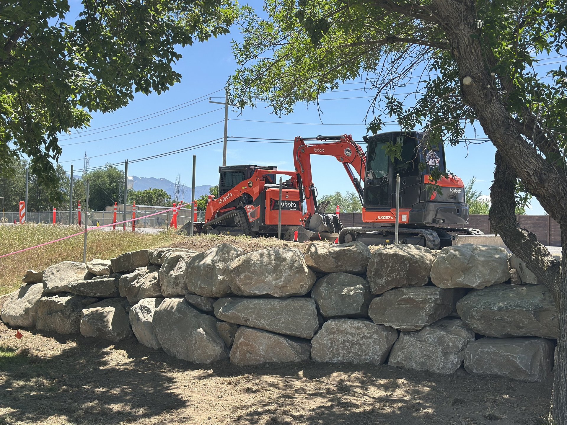 Boulder wall with Kubota skid steer and excavator sitting idle