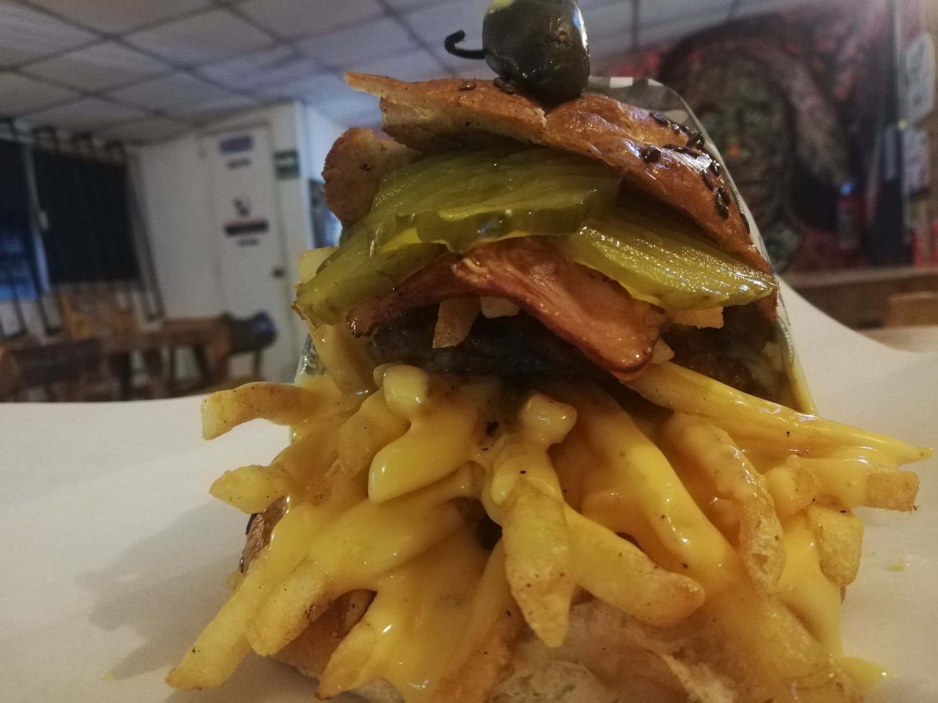 Hamburguesa gourmet con tocino, pepinillos y papas fritas crujientes bañadas en salsa de queso.
