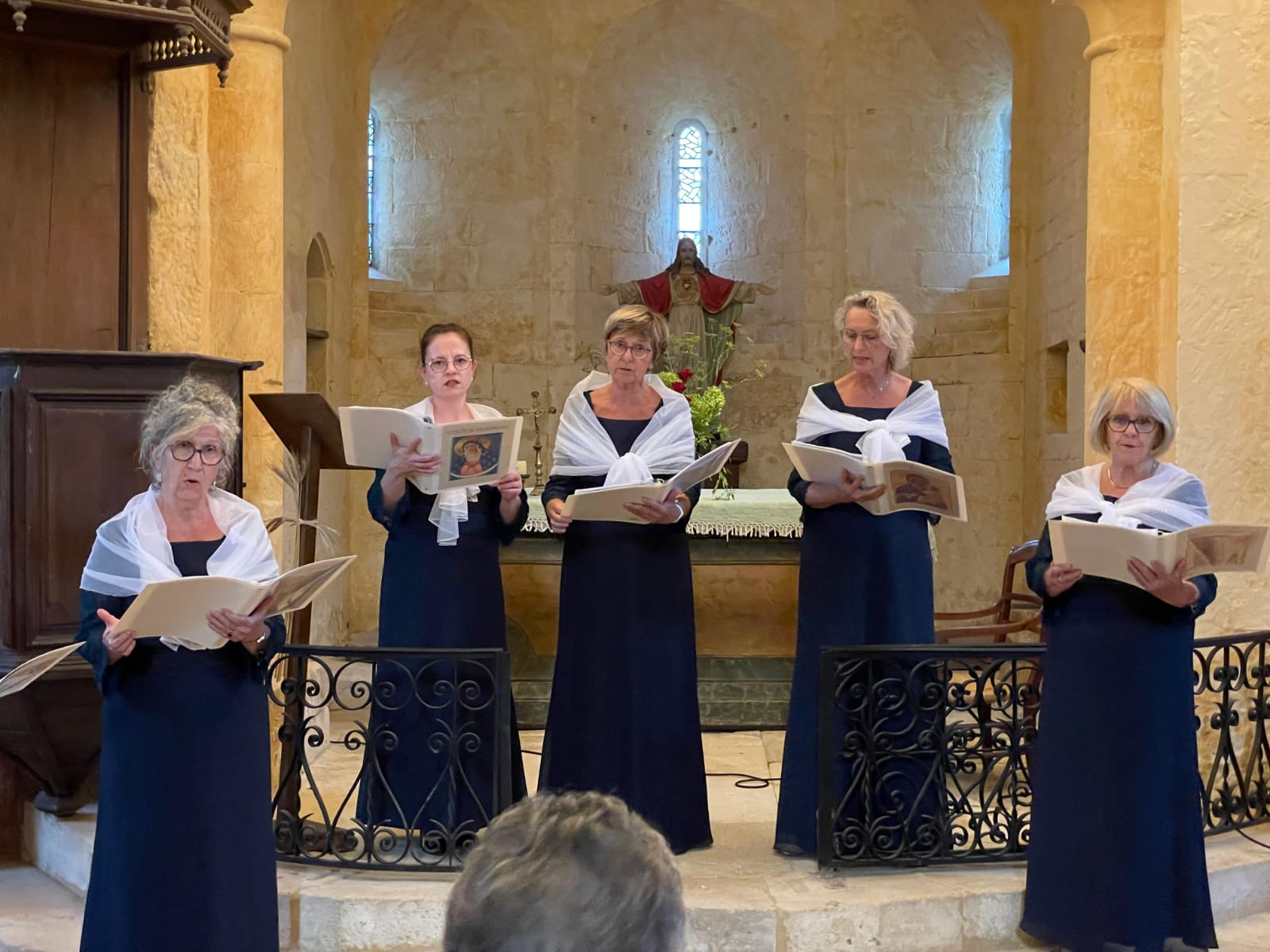 A women's vocal ensemble wearing blue gowns performing choral music inside a historic stone church.