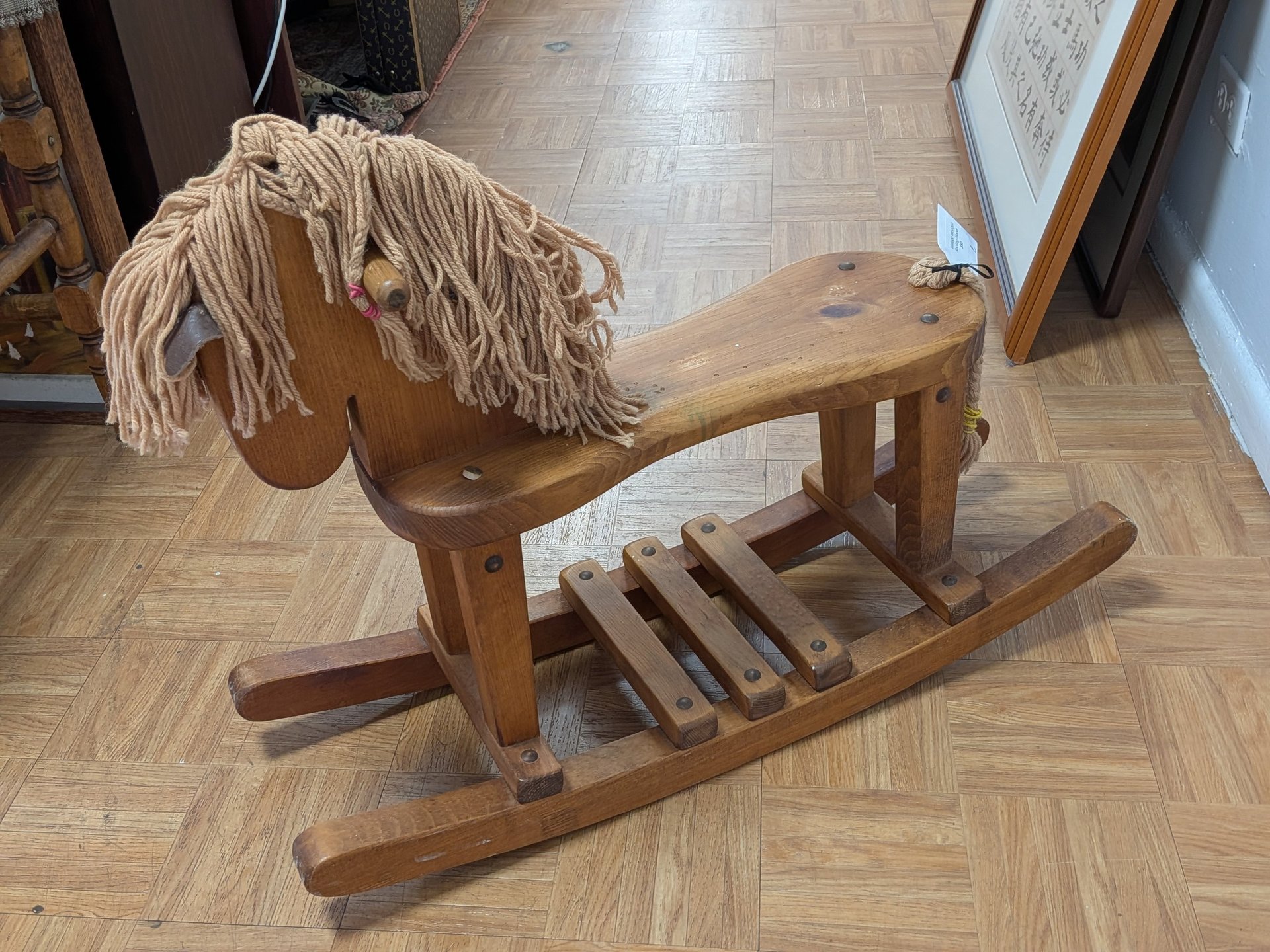 Vintage wooden rocking horse toy with yarn mane on a parquet floor.