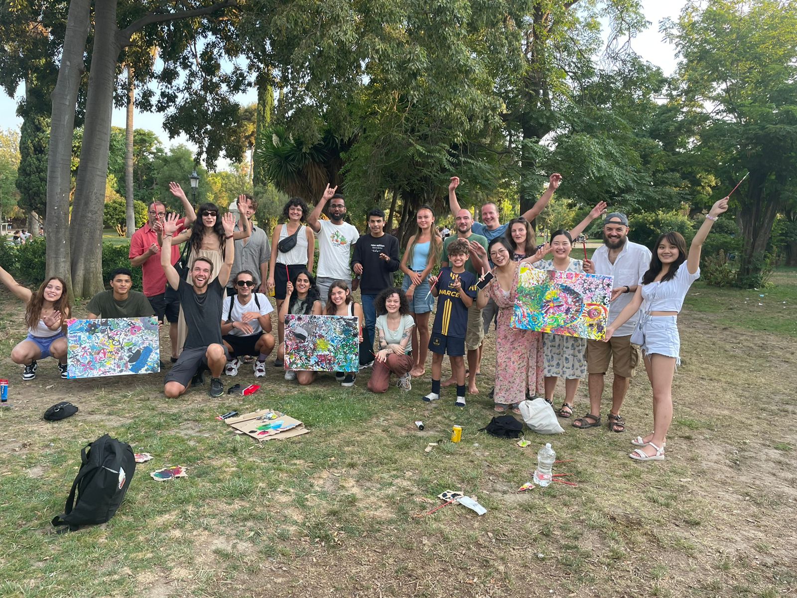 Des amis souriants tiennent des tableaux abstraits lors d’un événement artistique dans un parc