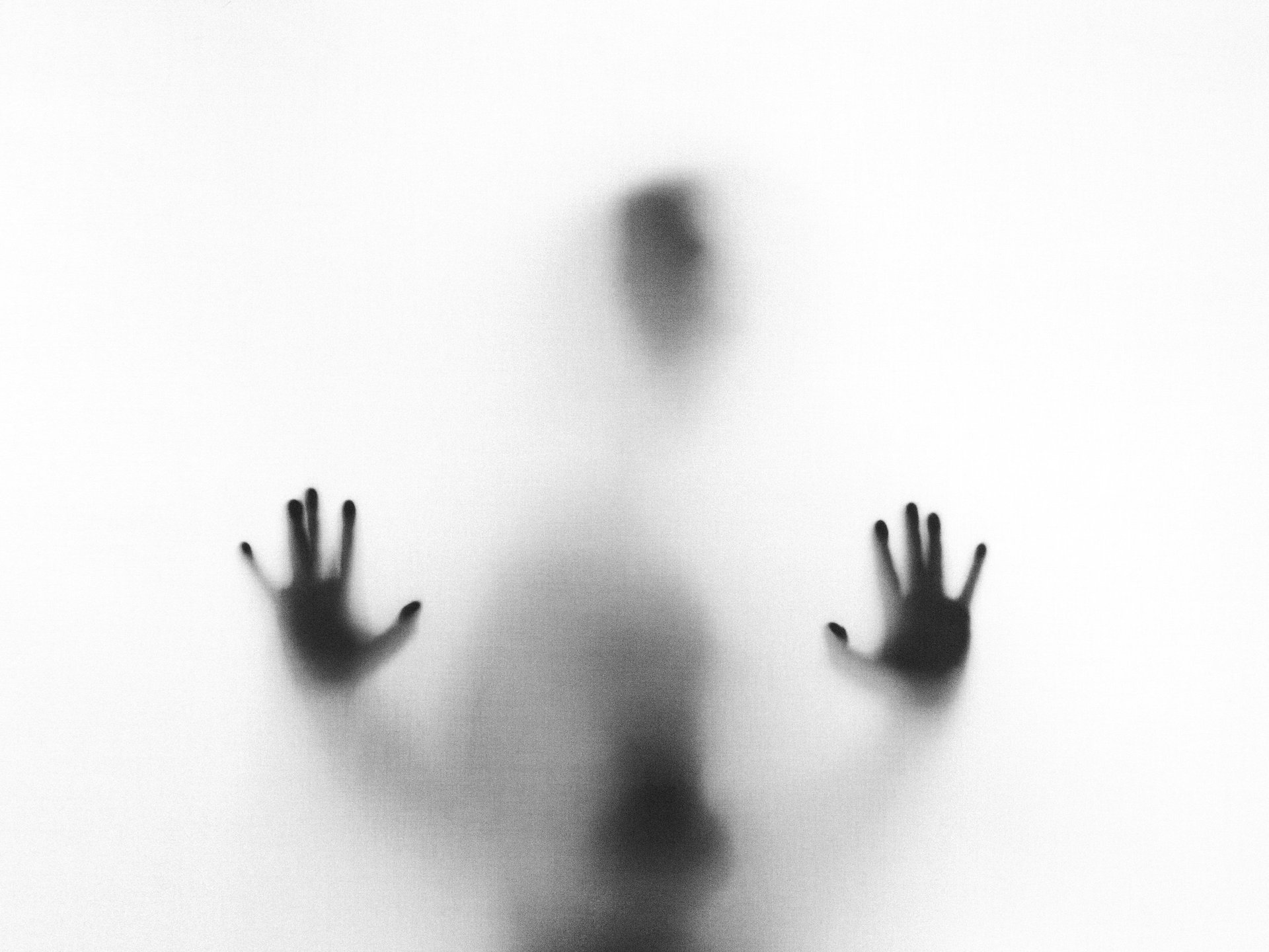 Eerie blurry silhouette of a person pressing their hands against a frosted glass surface.