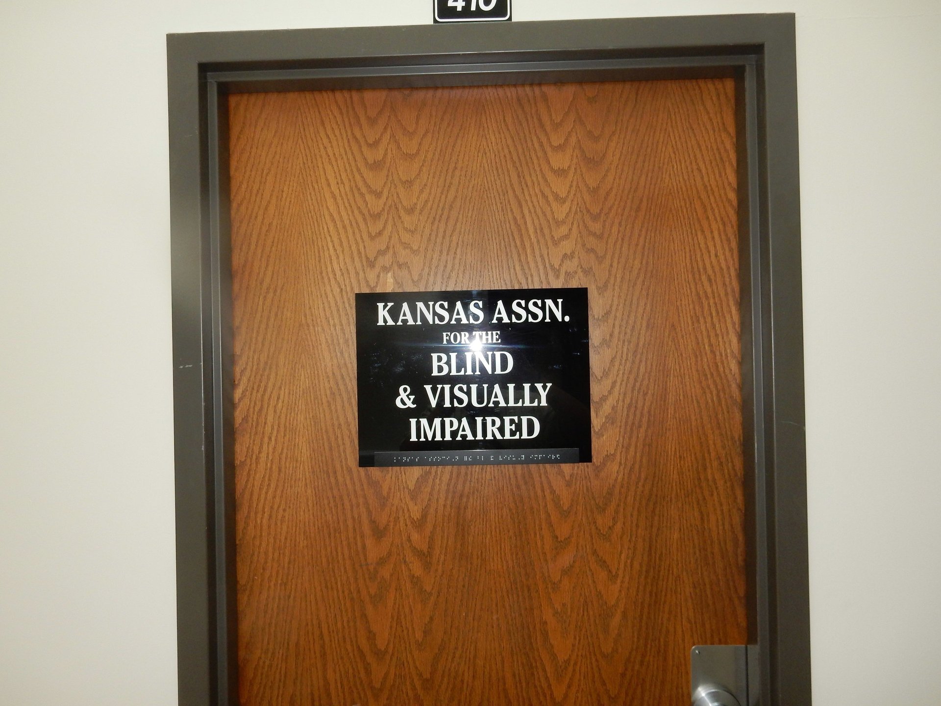 "A wooden office door with a black sign that reads 'KANSAS ASSN FOR THE BLIND & VISUALLY IMPAIRED