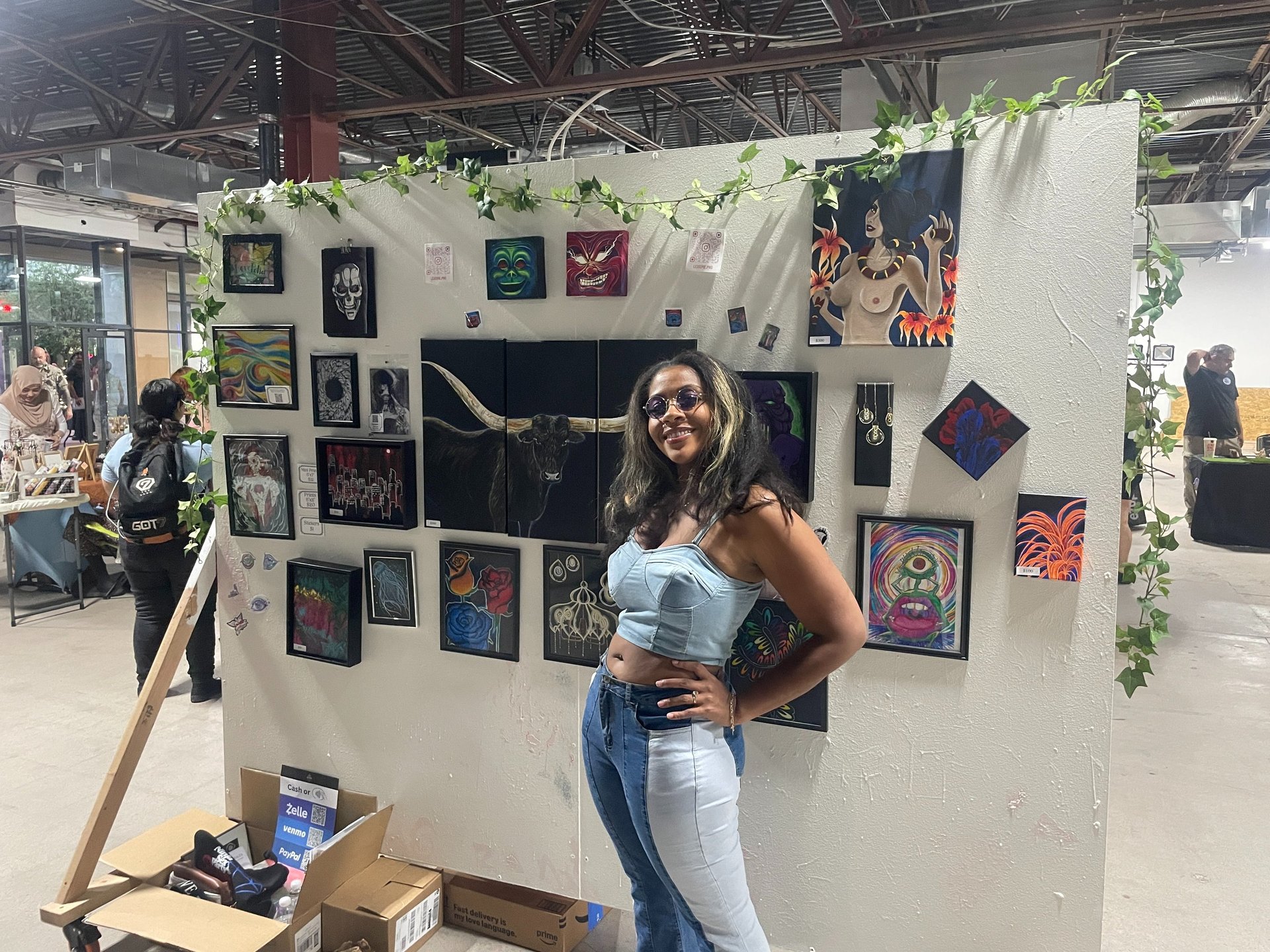 Alexis Peralta the artist standing in front of her wall of art at a gallery tacosxart