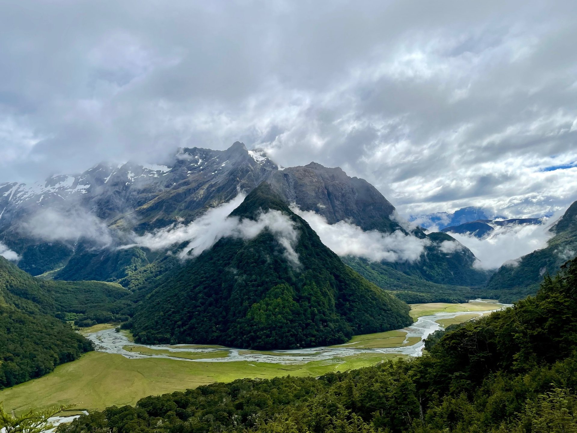 Spacious mountain scene with a river and clouds hanging near the tops.